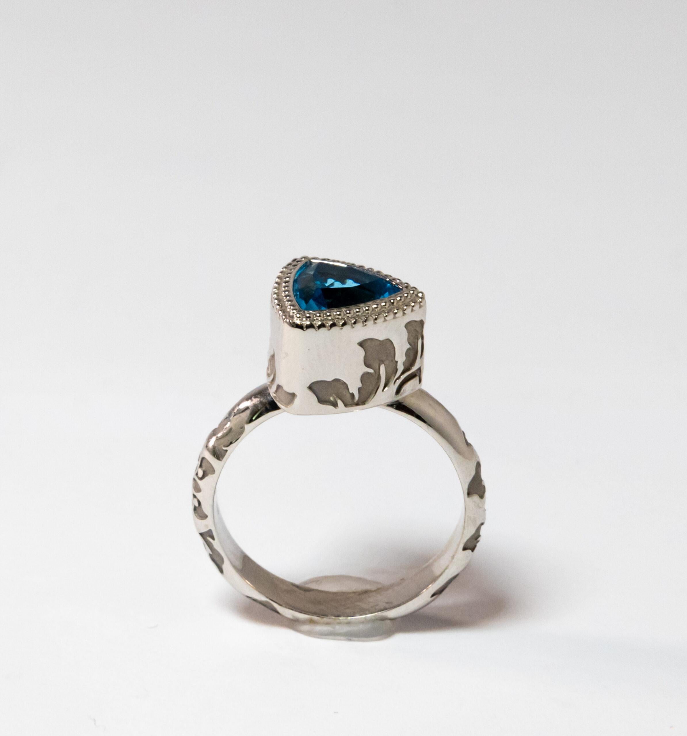 This ring is made of 18K White Gold. It is decorated with floral engravings and triangle-cut Blue Topaz (~ 2.02ct).

Size – 55 (7 US)