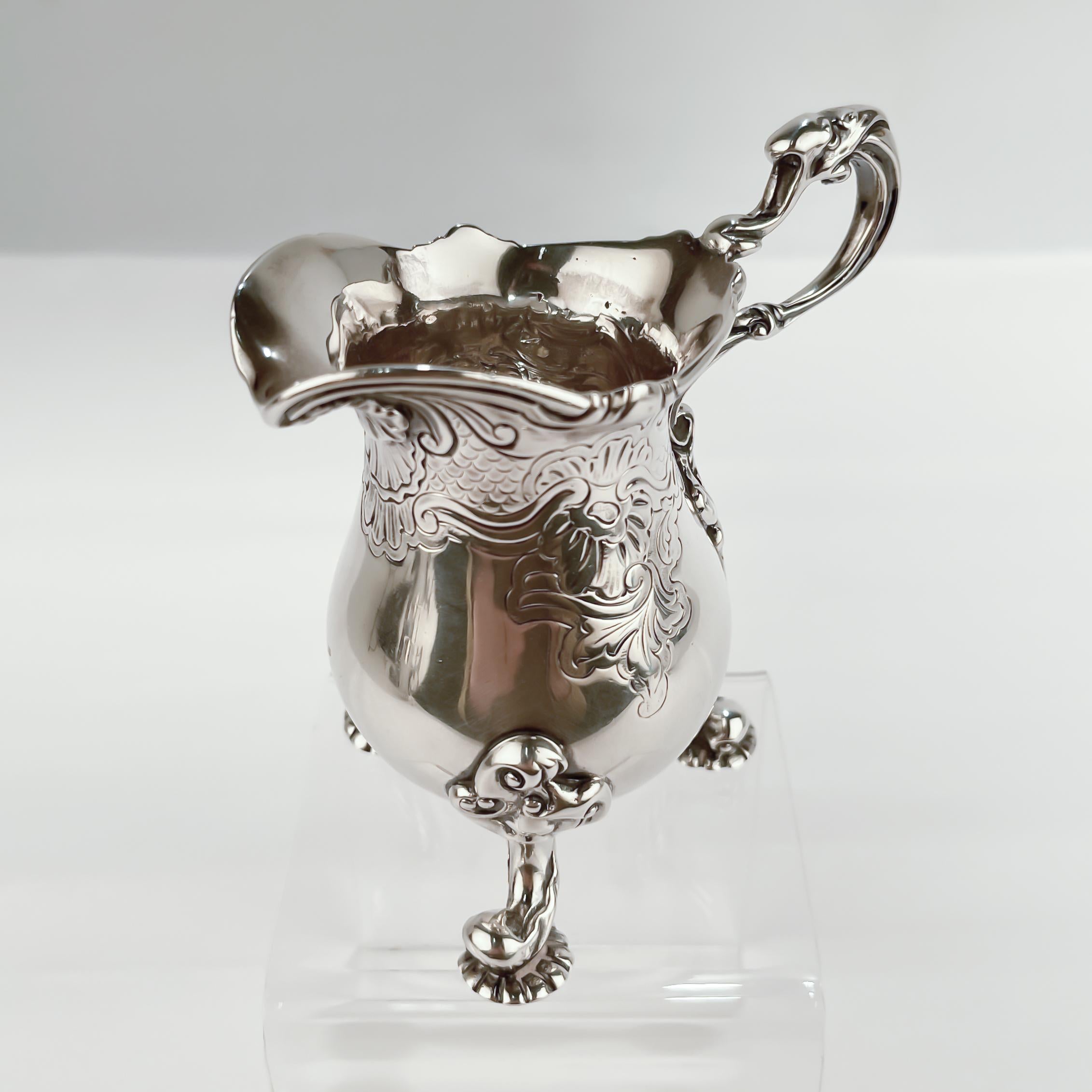 A very fine sterling silver creamer or milk pitcher.

By Carrington & Co. 

With an exuberant neo-Rococo (or George II style) design including etched scroll work and cells to the body, an applied shell device to the spout, a handle with a fantasy
