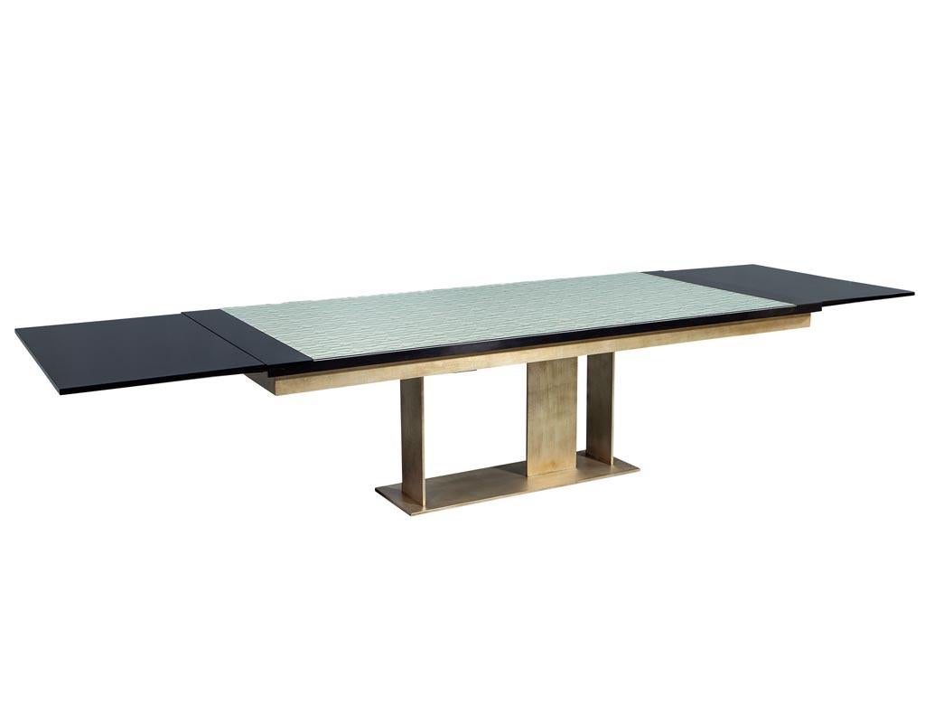 Carrocel custom modern glass top dining table with brass base. Custom-made dining table, styled with a modern brass base flowing into a textured glass top, glass is smooth on top, texture is underneath. Table has black lacquered accent ends with