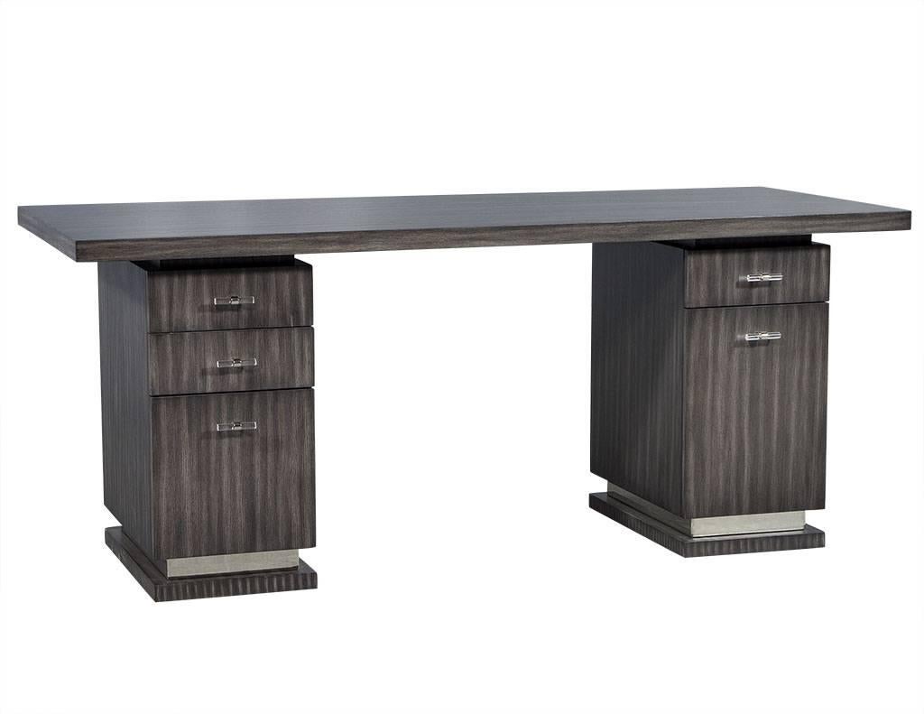 This modern writing desk has coastal flair.  Finished in a weathered grey, it has two base cabinets with an inset section at the top of each base under the table top. The left side has three drawers, two at the top, and a deep bottom that can hold