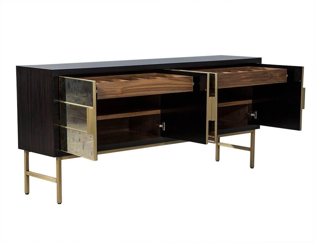 This modern console is made to order. Crafted out of solid walnut, this piece is highlighted with custom antiqued mirror sections and adorned with gold metal vertical handles. There are four doors total that conceal two wide lined drawers and two
