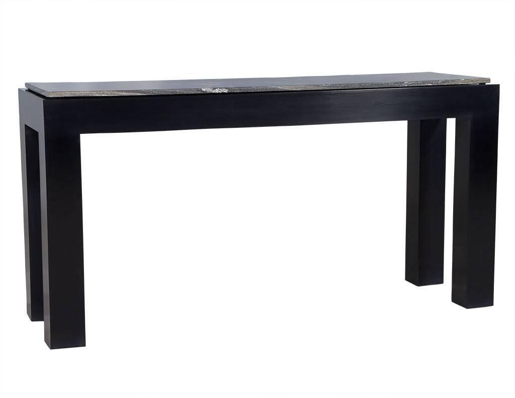 This modern console is made to order. The black lacquered wood base sits atop large, square legs and is topped with a large slab of marble. The marble piece is a flawless blend of black, grey and white, and is smaller than the top surface of the
