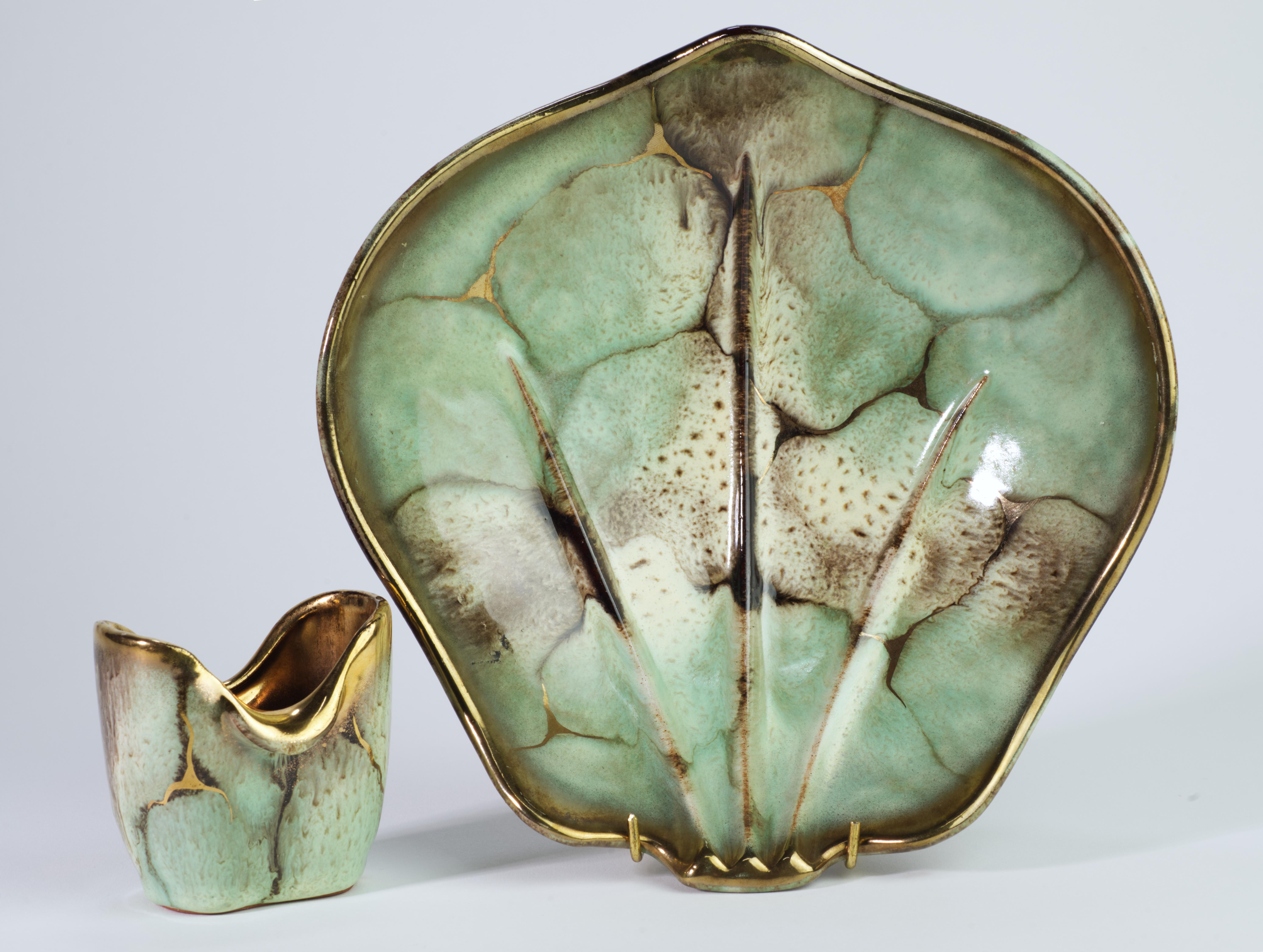  Il set composto da una ciotola e da un piccolo vaso o bocciolo è stato realizzato da Carstens Tönnieshof con un complesso smalto verde acqua, beige e oro. La ciotola ha uno smalto nero monocromatico sulla superficie inferiore, mentre il vaso ha uno
