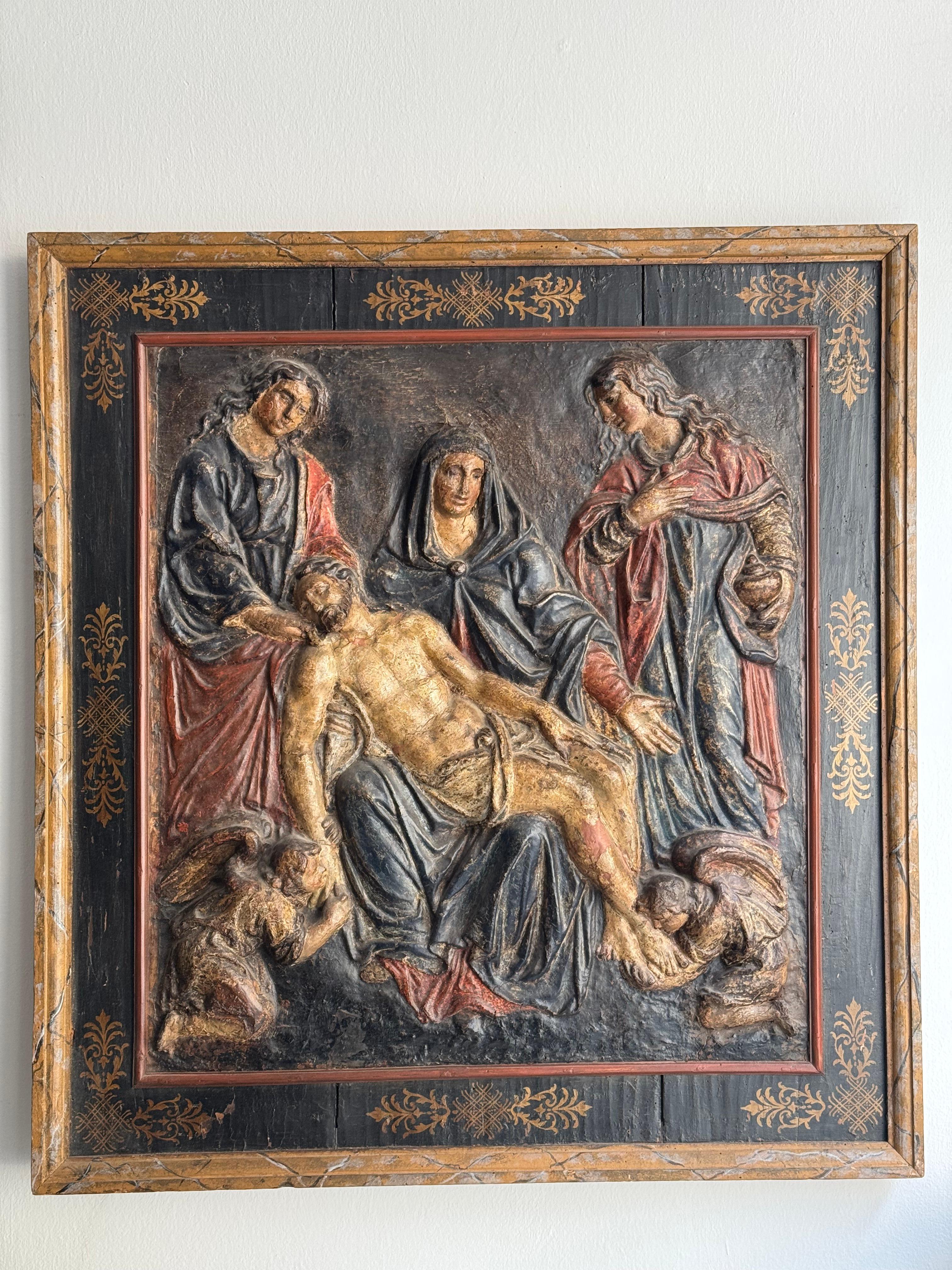 Carta pesta policroma raffigurante la Deposizione di Cristo con cornice in legno decorata coeva. 
Manifattura toscana del XVII secolo.
L'opera mostra il corpo di Cristo morto sorretto da figure sofferenti, identificabili con la Vergine Maria e la