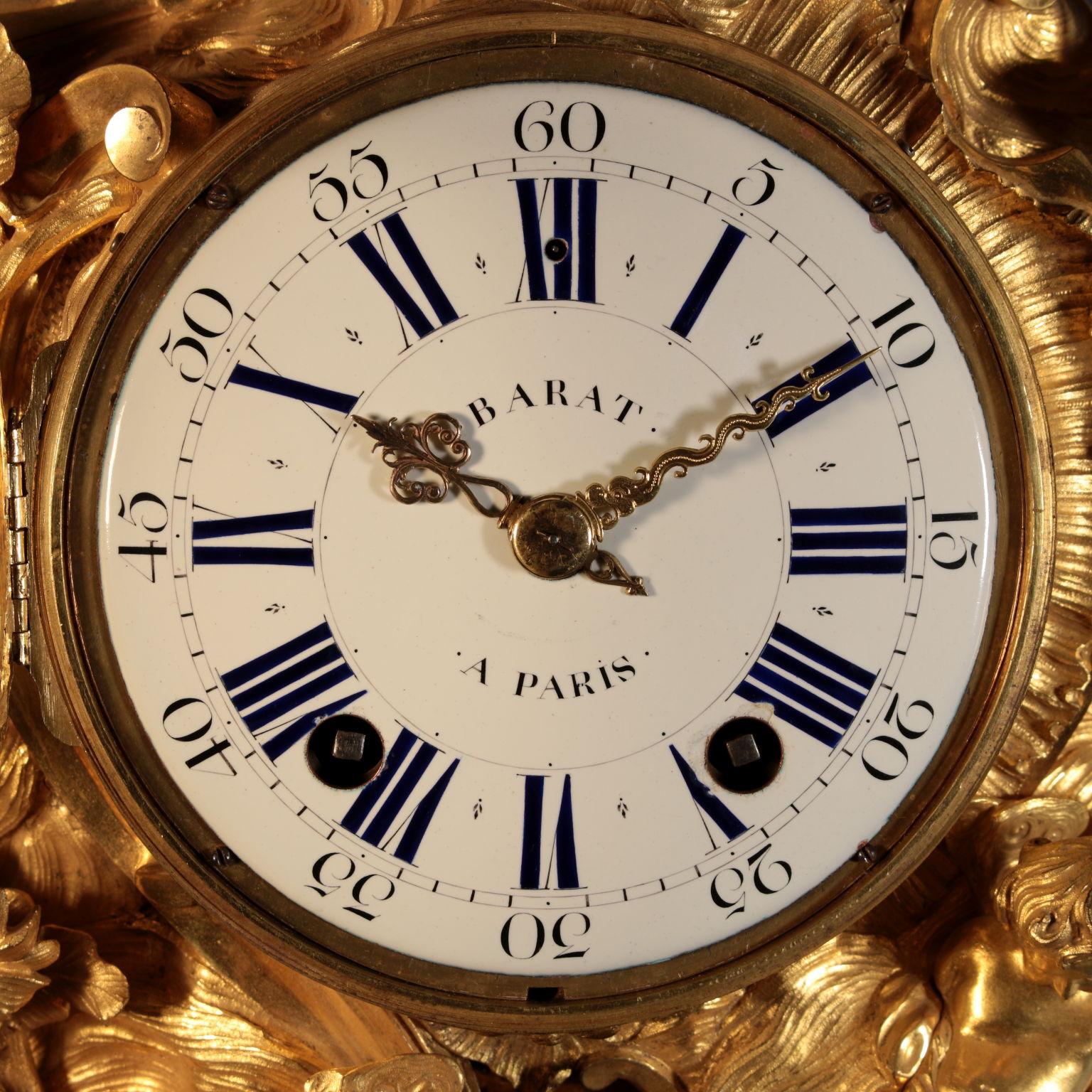 Cartel clock from the Louis XV period, gilded and chiseled bronze.
The clock has a marked asymmetrical structure, typical of the Louis XV era.
The dial is circular, enamel painted in the shades of blue and black, and it is signed 