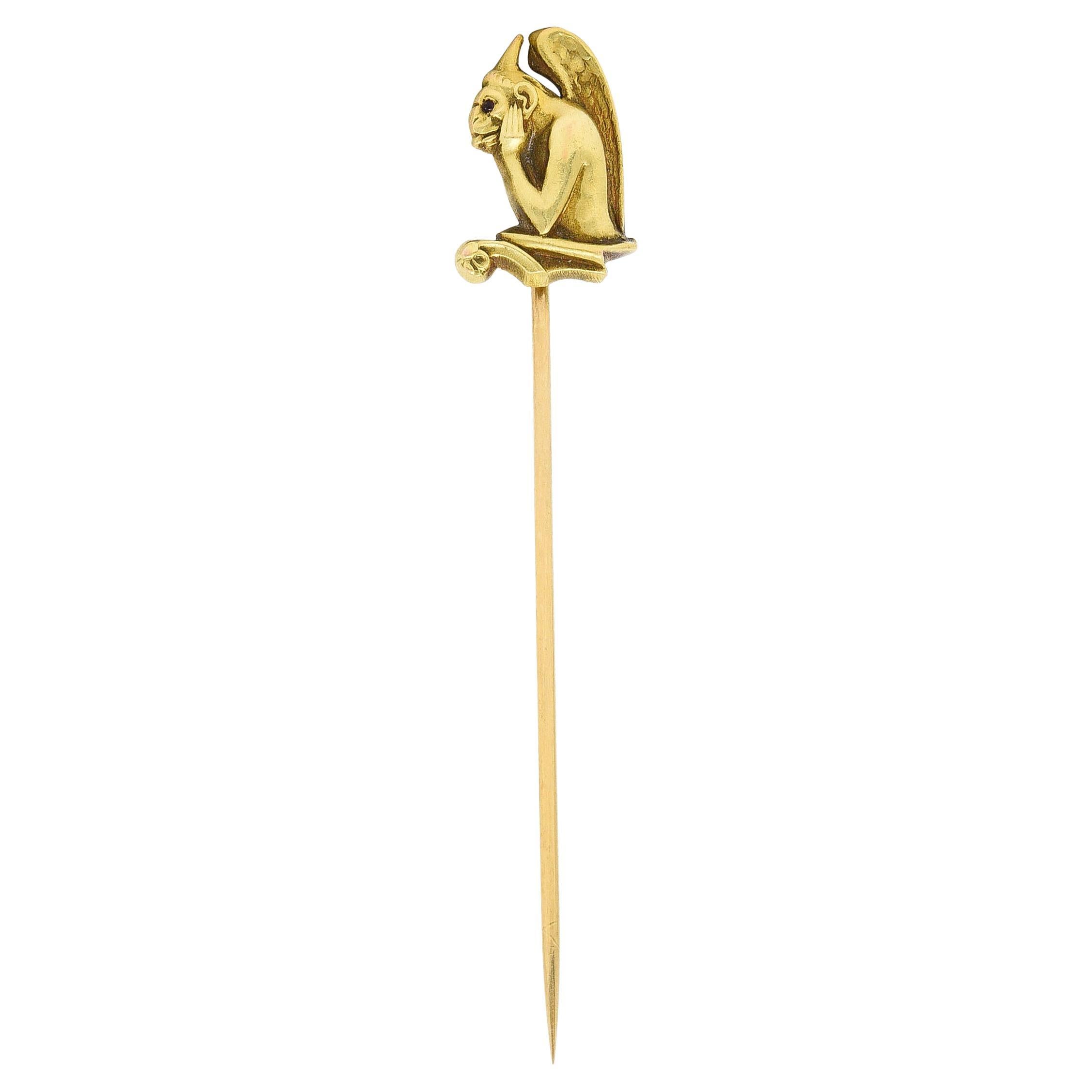 Stickpin designed as the profile of a winged gargoyle resting head in hands 

With textured wings, hair, and stylized features

Accented by round cabochon garnet eye

Stamped 14k for 14 karat gold

Maker's mark for Carter Gough & Co.

Circa: