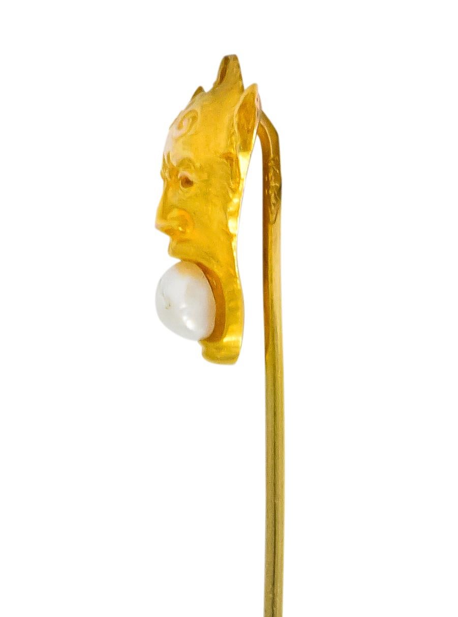 Depicting the stylized face of the Greek god Pan with long ears and curved horn design on forehead

With open mouth holding a baroque pearl, white body color with silver and yellow overtones

Maker's mark for Carter Gough & Co. and stamped 14k for