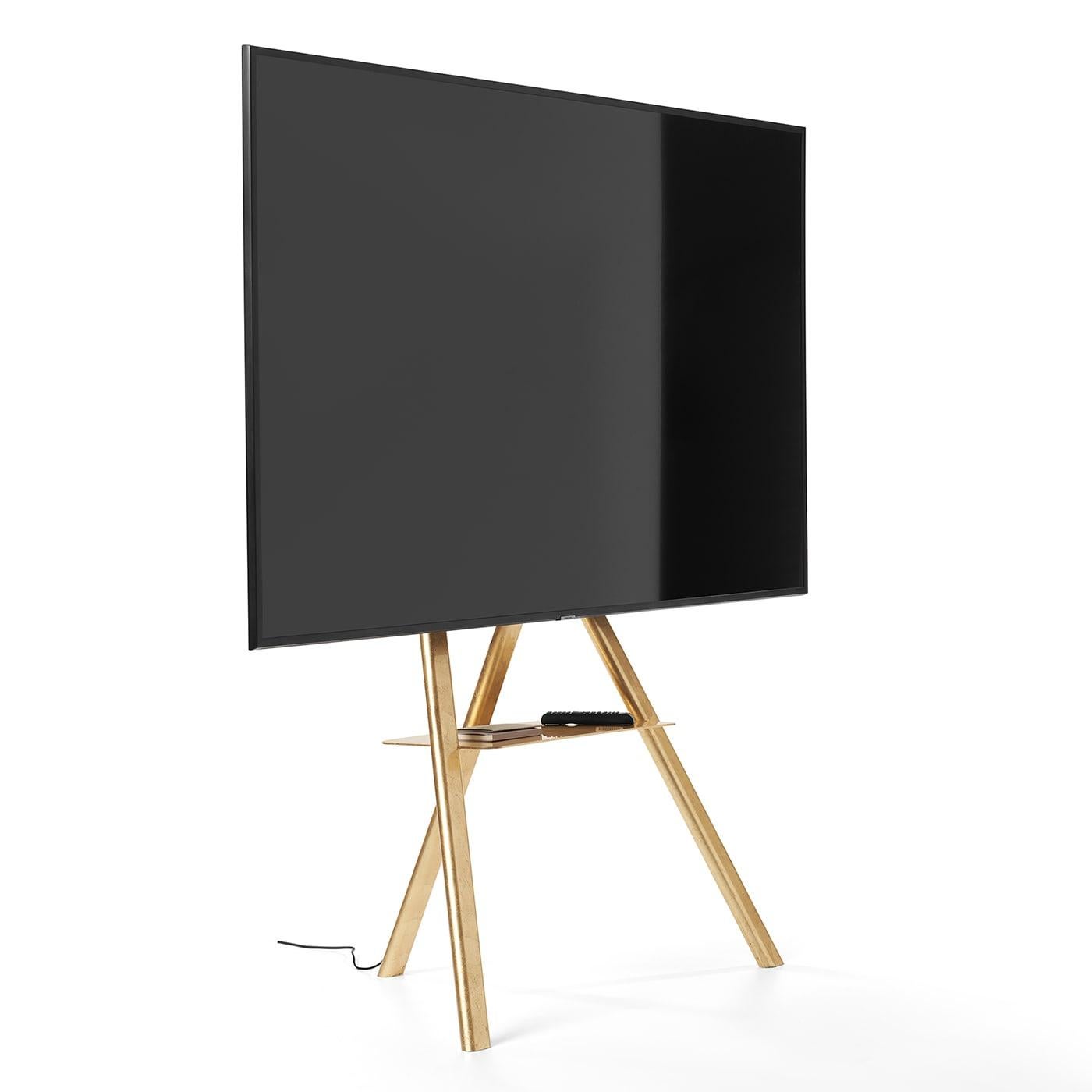 This superb steel tripod pairs the minimalist rigor of its clean lines with the luxe appeal of its sublime finish of polished gold leaf. Equipped with a practical shelf, it features a black frame element that can be fitted to smart TVs ( from 43