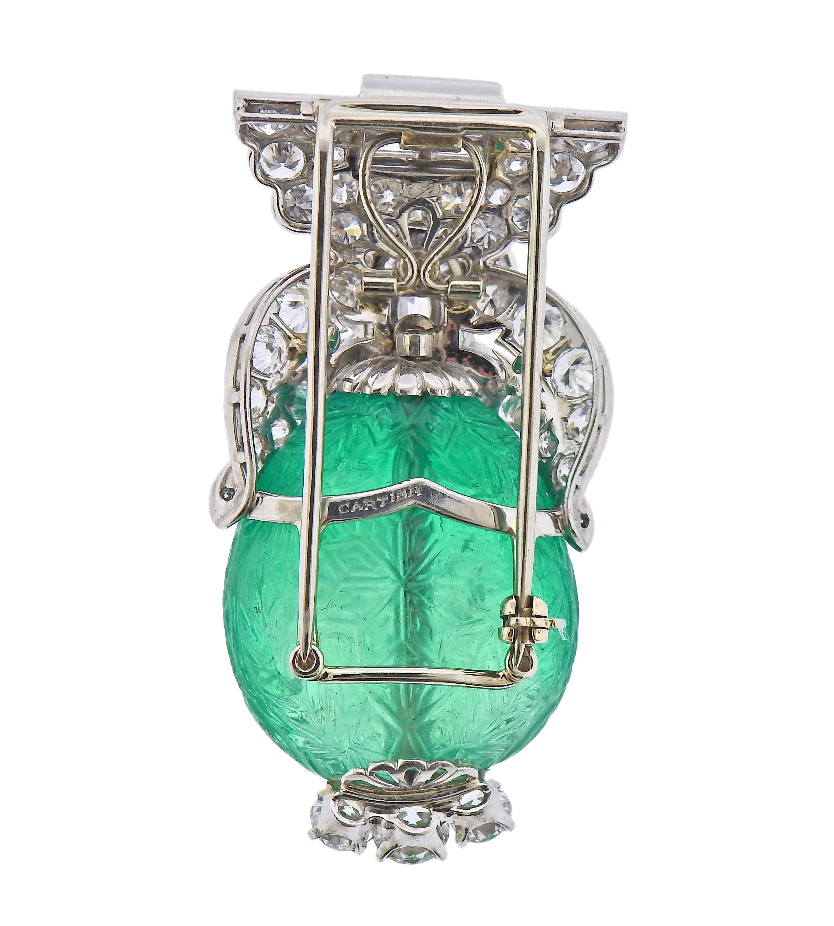 Exquisite platinum Cartier brooch, set with an approx. 65 carat carved emerald, measuring 25mm x 25mm x 11.4mm, surrounded with a total of approx. 7.50-8.00 carats in diamonds. Center marquise diamond is approx. 1.51ct . Brooch measures 52mm x 28mm.
