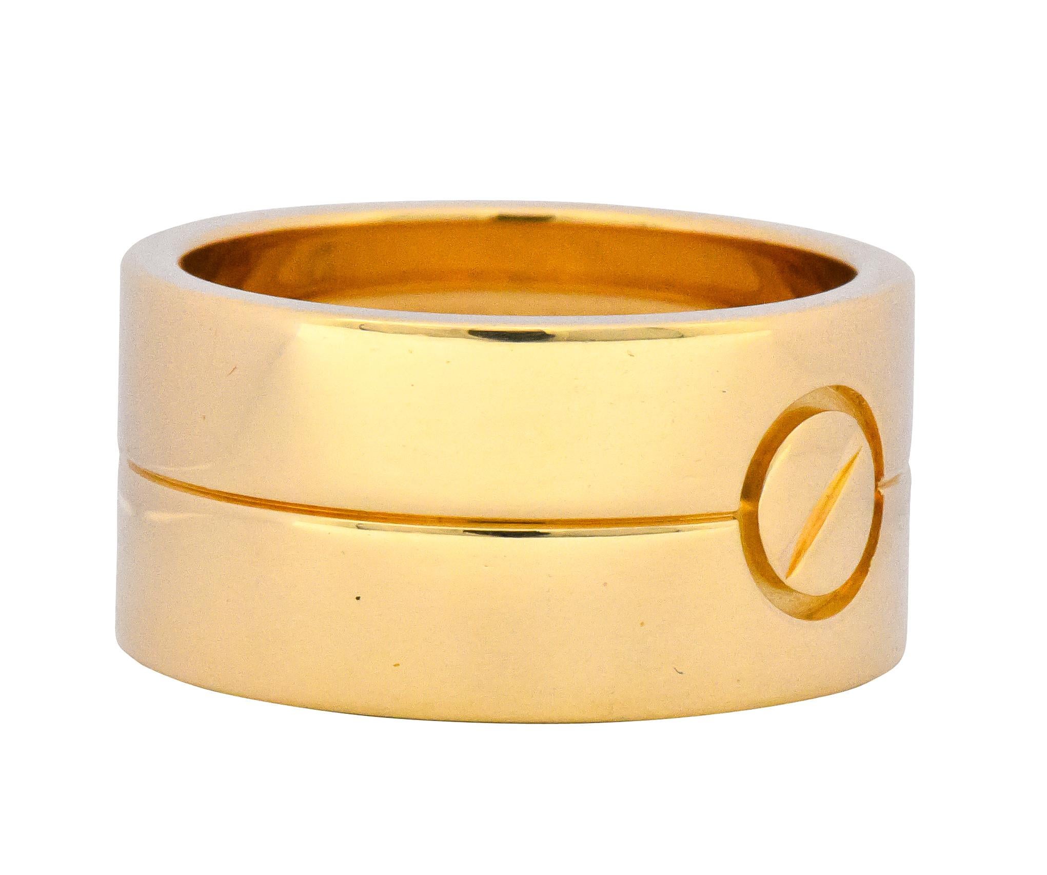 Wide gold band, centering the Cartier Love symbol

Etched line bisecting the ring

Fully signed Cartier, numbered, with maker's mark, stamped 62, 750 and BT and assay marks

Ring Size: 10 & Not Sizable

Top measures 11.8 mm and sits 1.8 mm