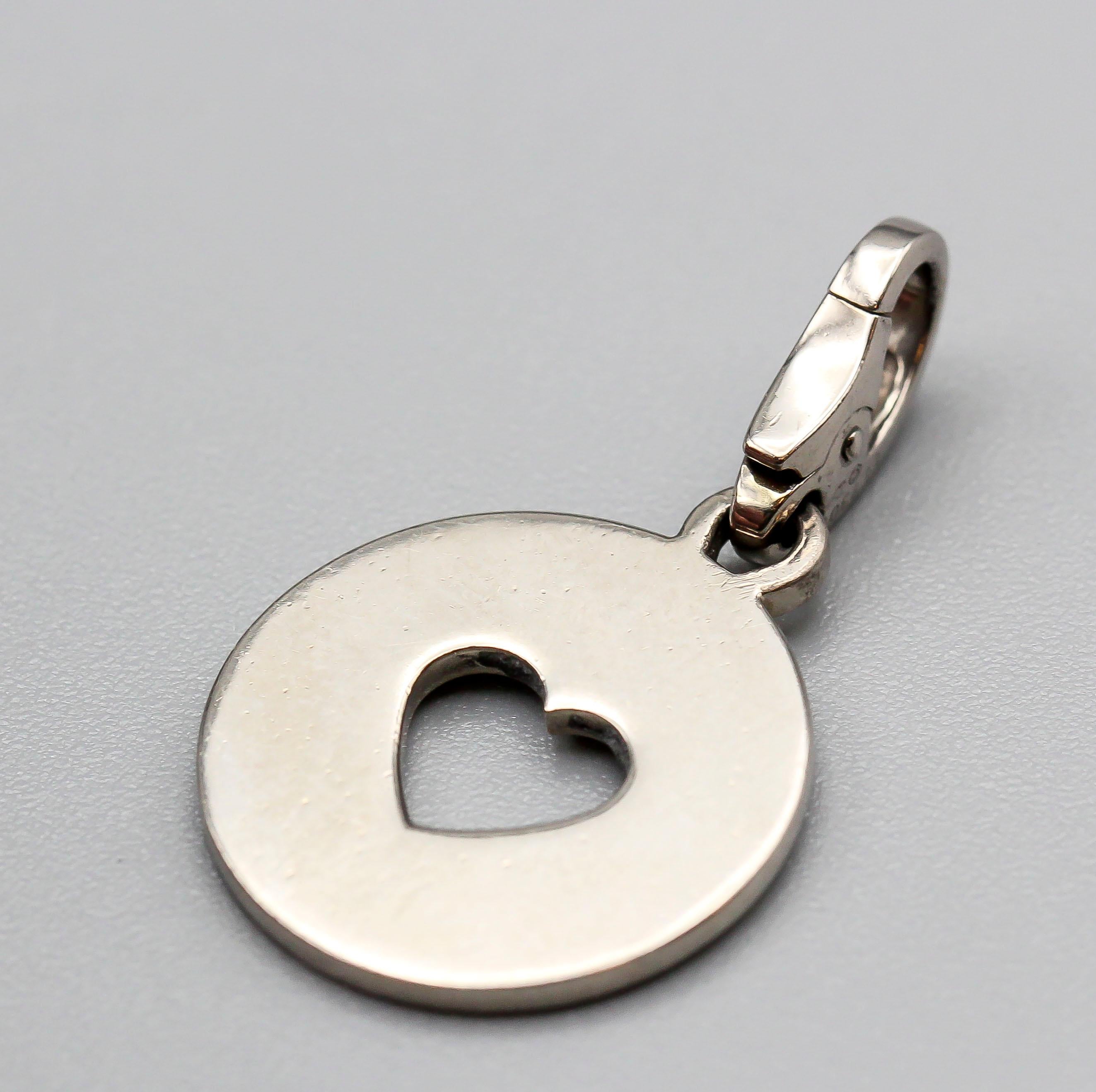 Fine 18K white gold charm by Cartier. It features a round charm with a heart shaped cut out.   Well made and easy to add to any bracelet or pendant.

Hallmarks: Cartier, 750 reference numbers