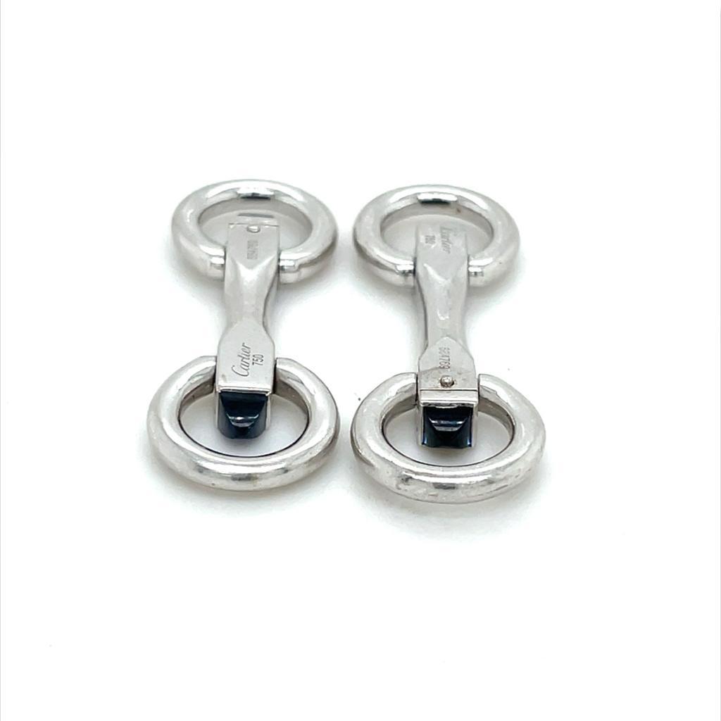A pair of Cartier 18 karat white gold stirrup cufflinks, circa 2000

Finished with a domed rich blue cabochon cut sapphire to either end of the hinges.

The solid and secure polished white gold circular folding fittings make these cufflinks very
