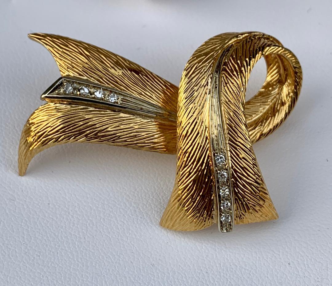 Very flowing, three dimensional, stylized ribbon or scarf design brooch pin by esteemed French designer, Cartier, is depicted in 18 karat yellow gold accented with rows of white diamonds down the middle of each side. Brooch could also be worn as a