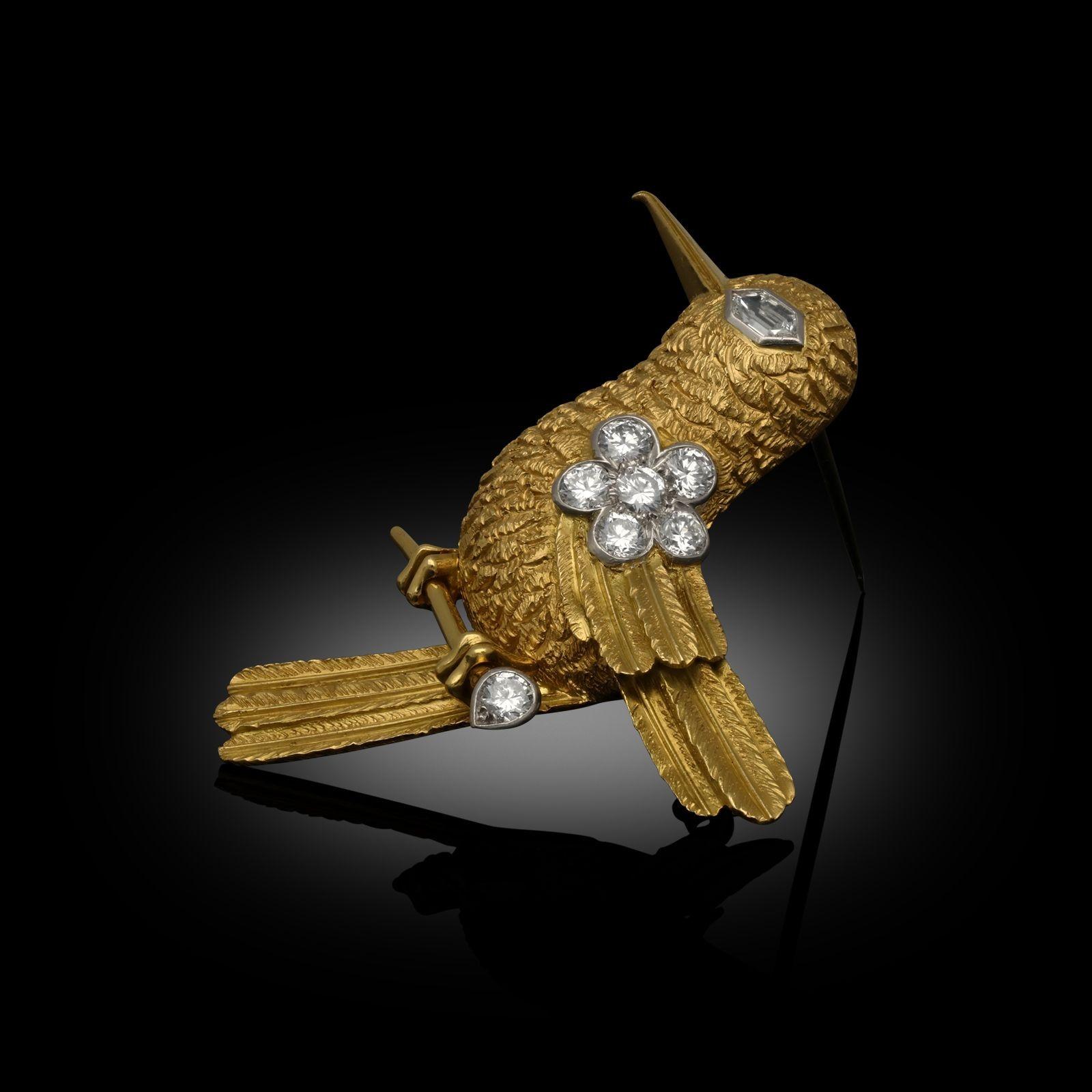 A charming gold and diamond stylised hummingbird brooch by Cartier c.1960s, the body finely modelled in 18ct yellow gold with a textured finish and carefully formed feathers, the beak and feet in polished gold, the eye set with a hexagonal shaped