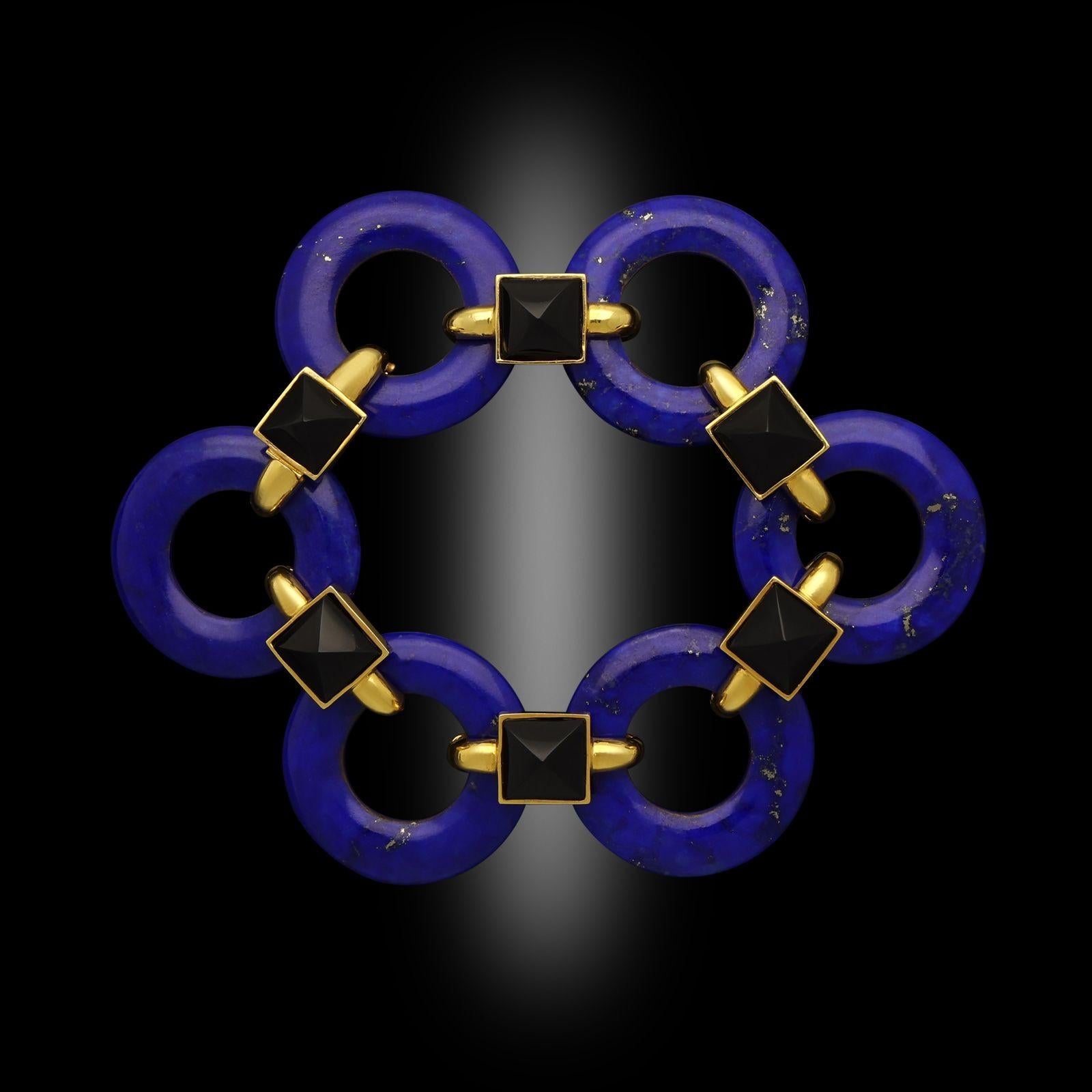 A bold and striking vintage bracelet by Cartier c.1970, designed by Aldo Cipullo the bracelet is formed of six uniform open circular rings of carved and polished lapis lazuli joined together via large oval 18ct yellow gold links each set to the top