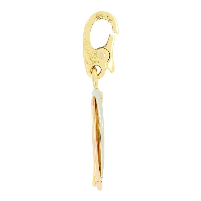 Creato in oro giallo 18 carati, questo charme è stato realizzato da Cartier. Al centro del charme si trova un motivo a croce, circondato dall'iconica trilogia di anelli in metallo di Cartier. Il pezzo misura 30 mm per 17 mm e pesa 5,2 grammi. I