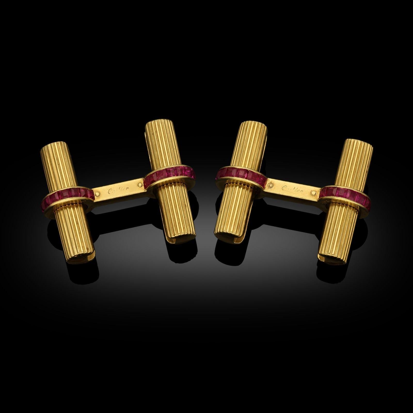 A pair of 18ct yellow gold double sided baton cufflinks by Cartier c.1960. The batons are fluted cylindrical bars in 18ct yellow gold, the connecting bars set with channel-set calibrated rubies. One baton on each is detachable by the twist and pull