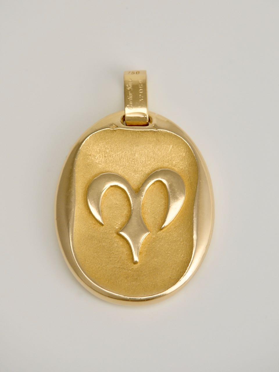 A heavy double sided 18k yellow gold Zodiac pendant for Aries (March 21 - April 19) showing a Ram leaping against a flame motif background and, to the reverse, a stylised astrological symbol of a Ram's head against a granular textured ground, the