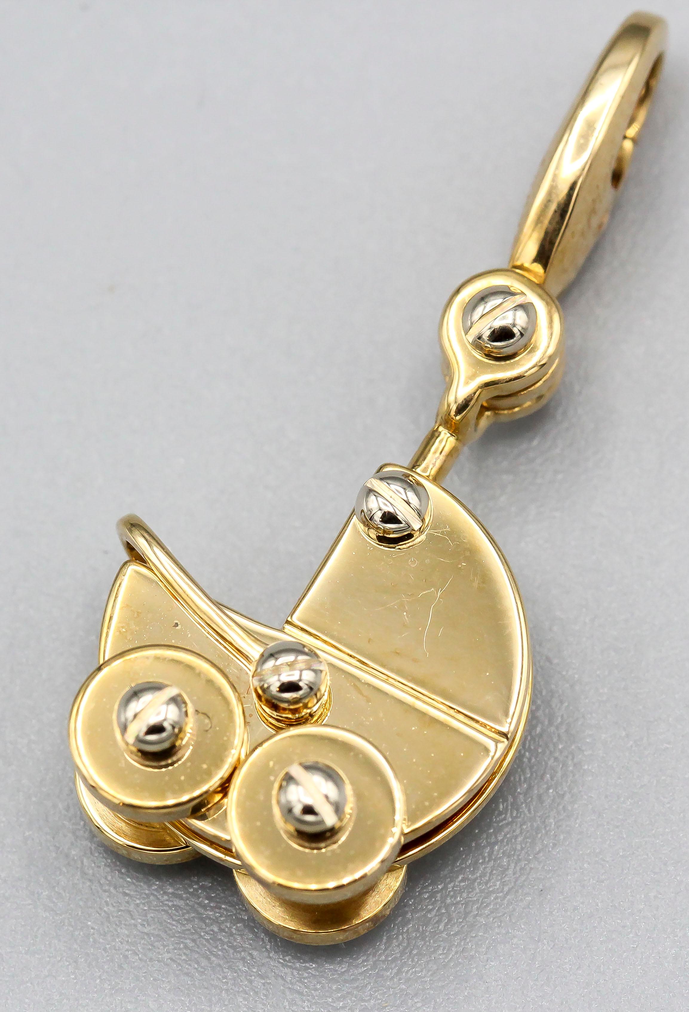 Fine 18K white and yellow gold charm pendant by Cartier. It resembles a baby carriage, which white gold accents.

Hallmarks: Cartier, 750, reference numbers, copyright, 2000.