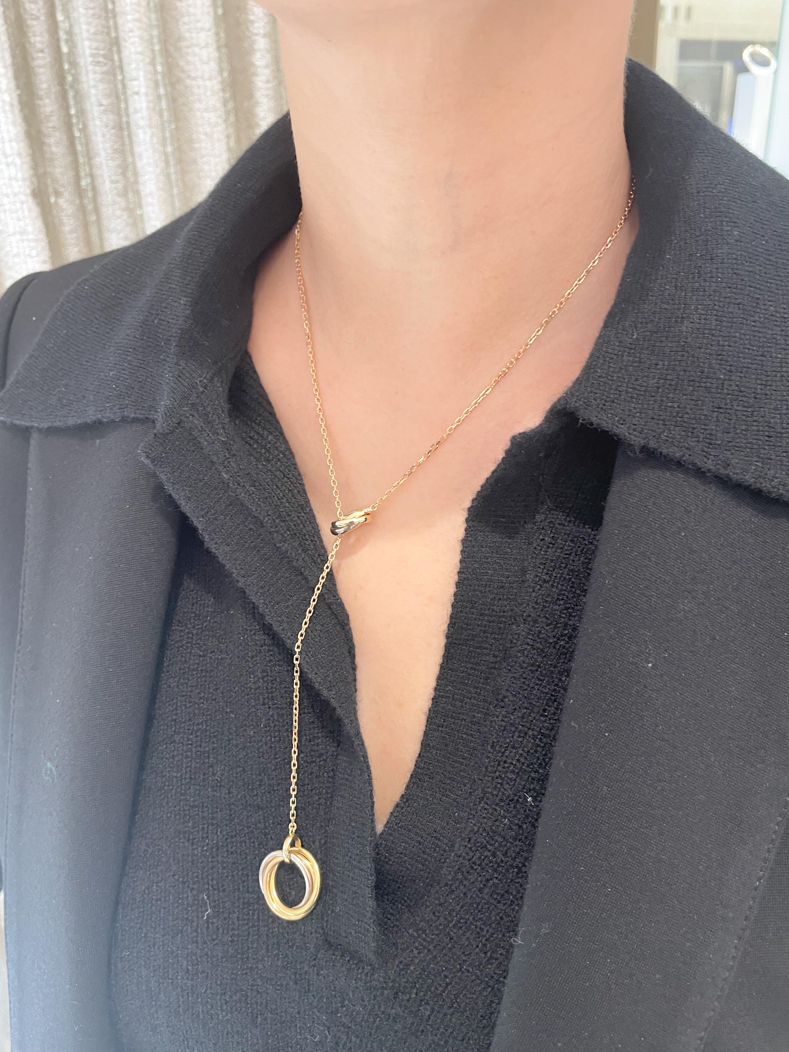 From designer Cartier, circa 2000’s, 18 karat yellow, white, and rose gold Trinity lariat necklace. This necklace is crafted with small oval trinity rings on one end of the necklace and round trinity rings on the other end. Both rings feature 53