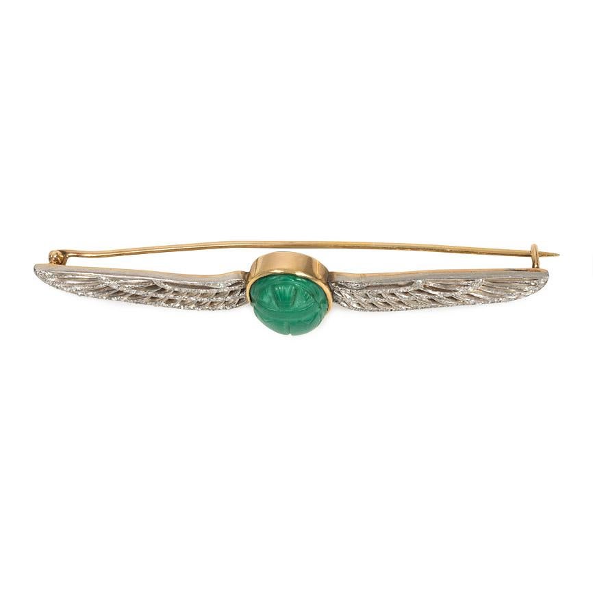 An Edwardian brooch in the Egyptian Revival style comprised of a faience scarab flanked by openwork diamond wings, in 14k gold and platinum. Cartier #0274