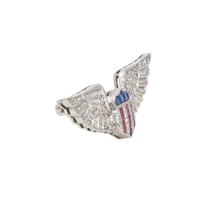 A Retro patriotic multi-gemstone brooch with pavé diamond wings framing a sapphire, ruby, and diamond shield, in palladium.  Cartier, #792.  Atw diamonds 1.00 ct.  Wing span approximately 2 inches