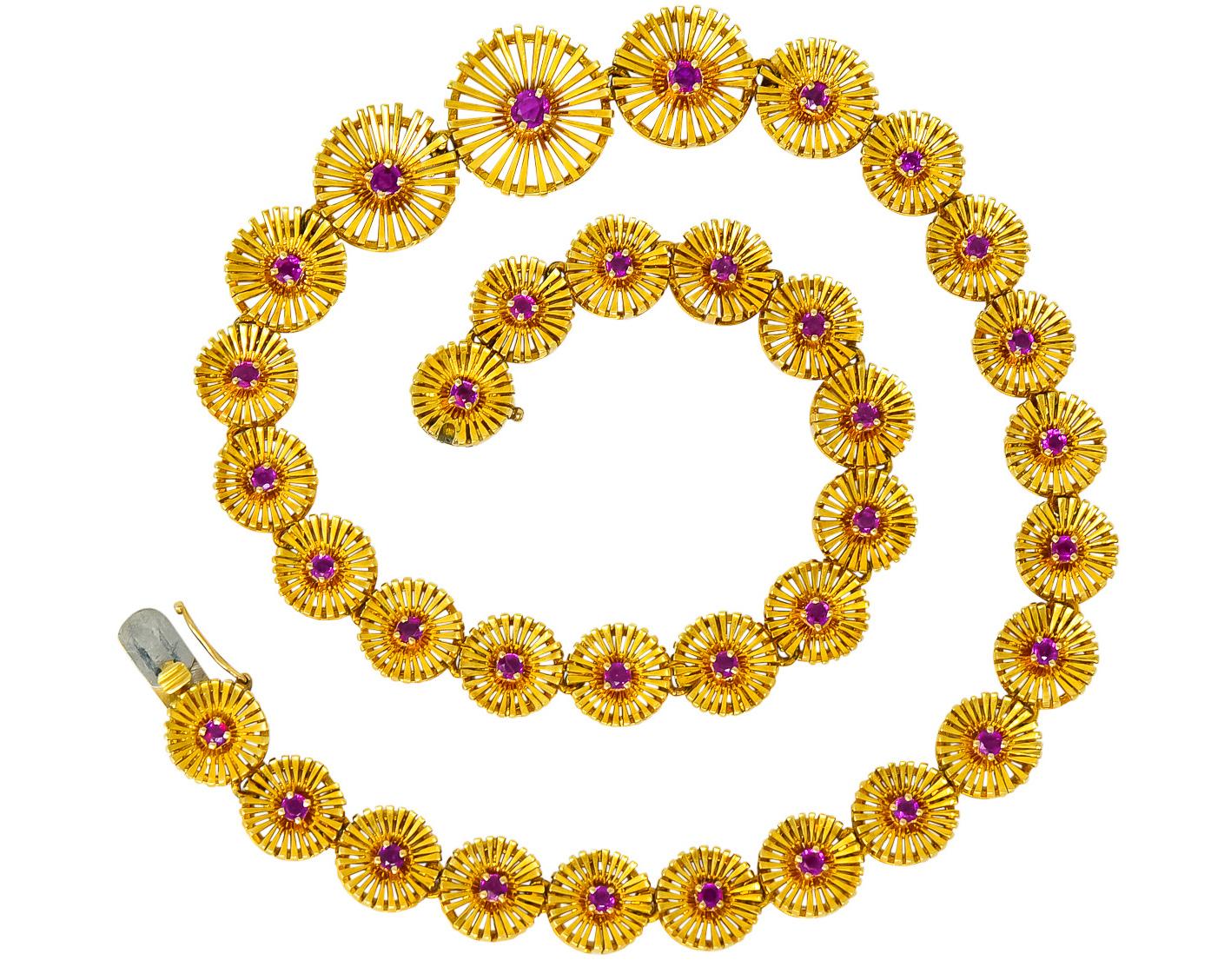 Collar style necklace with graduated flower links designed as radiating disks of polished gold

Each link centering a prong set round ruby, weighing approximately 2.50 carats, transparent pinkish-red in color and very well matched

Completed by