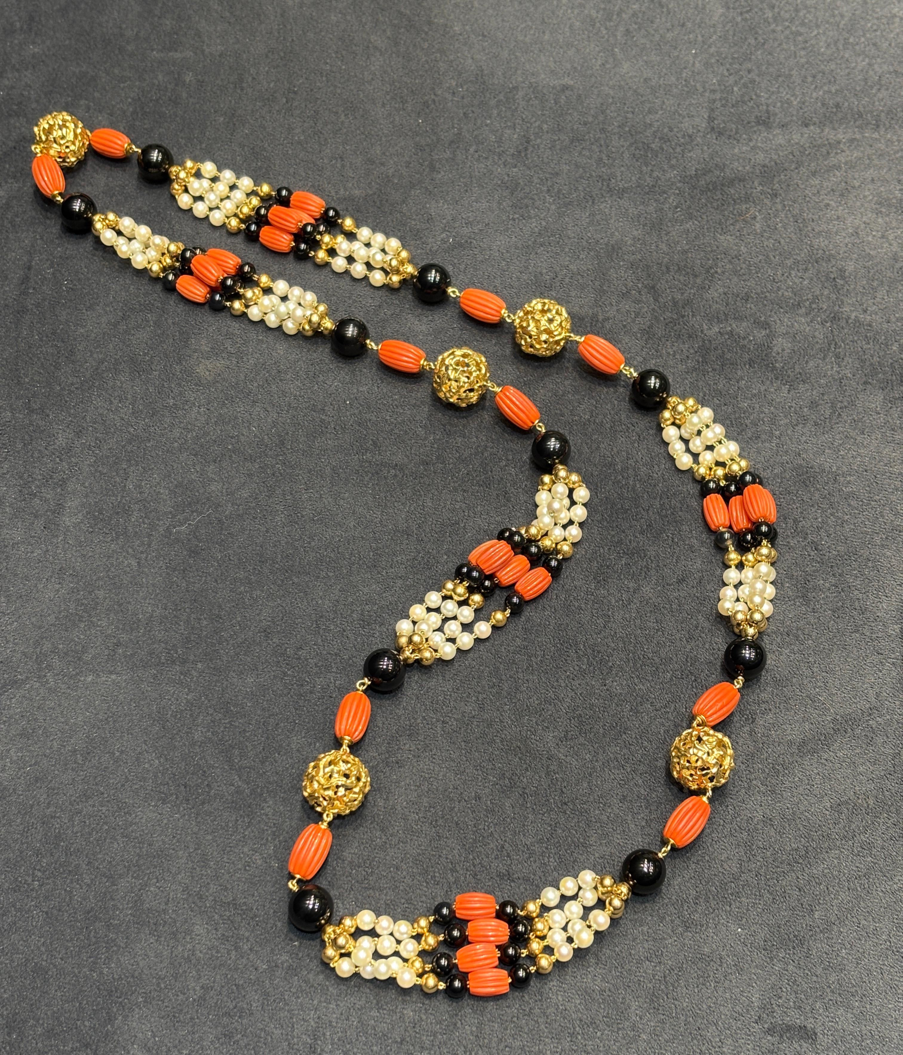 Questo elegante sautoire Cartier degli anni '70 è composto da onice, corallo, perle e sfere in oro 18 carati. Le sfere dorate misurano 20 mm di diametro, mentre le perle di onice più grandi misurano 12 mm di diametro. Il sautoire è abbastanza lungo