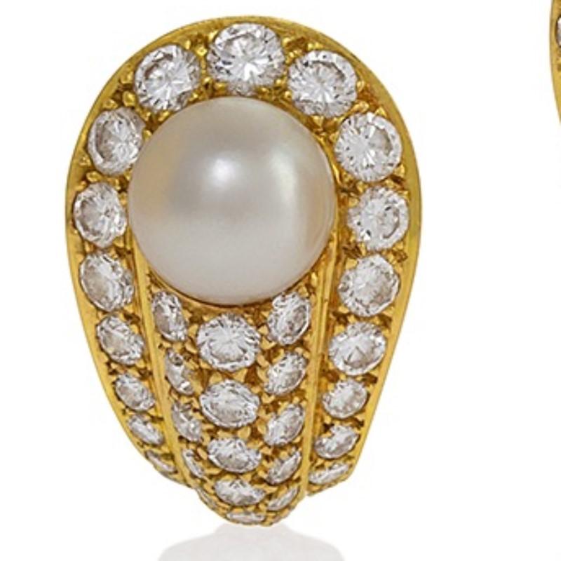 A pair of French Late-20th Century 18 karat gold earrings with pearls and diamonds by Cartier. The earrings each center on an 8 mm Japanese cultured pearl, surrounded by a total of 74 round brilliant-cut diamonds with an approximate total weight of
