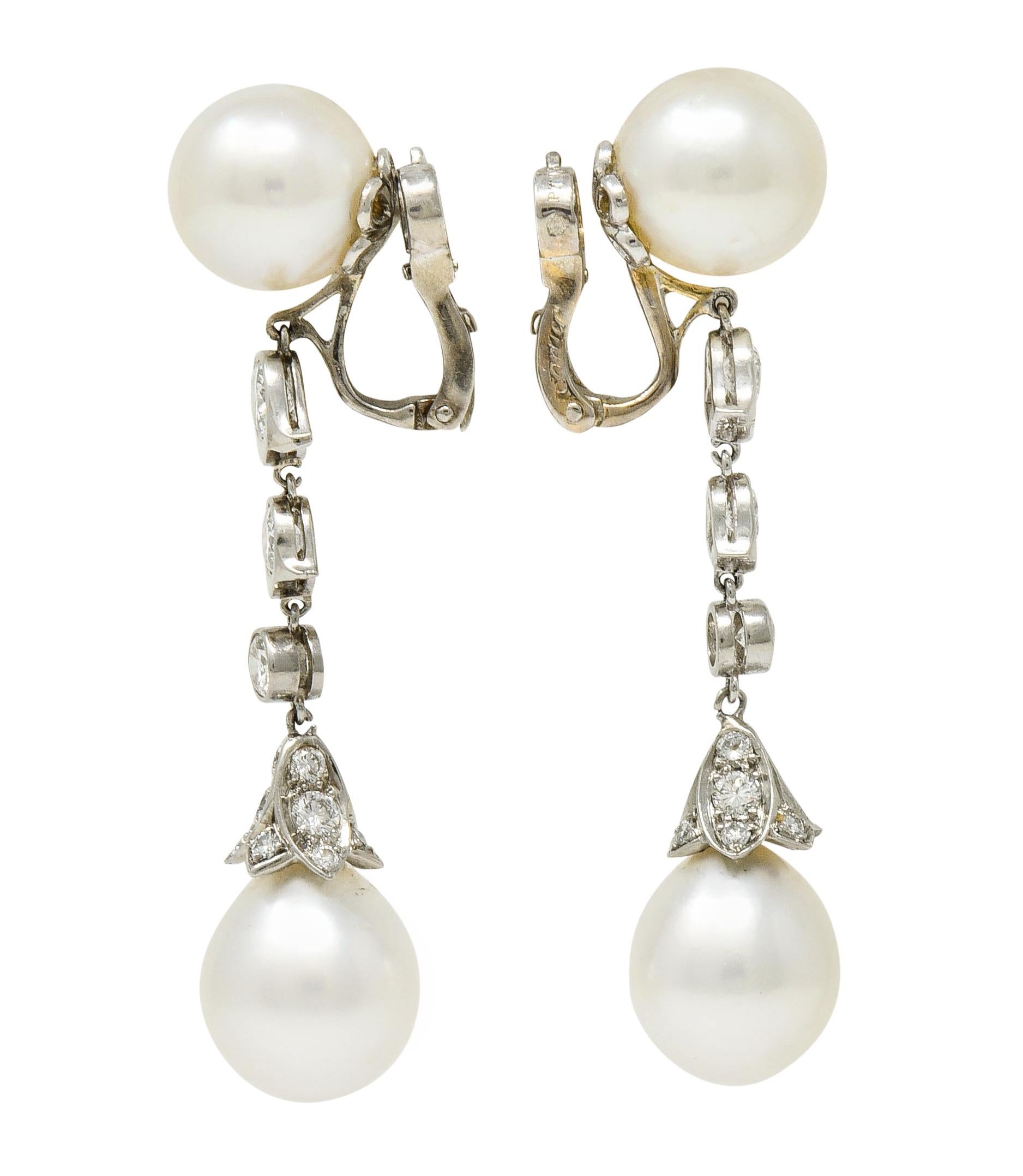 Drop earrings feature a 10.6 mm round South Sea pearl surmount, cream in body color with rosè overtones and excellent luster

Suspending stylized floral bezel links, articulated, and a pavè scalloped pearl cap; tested as platinum

Set with round