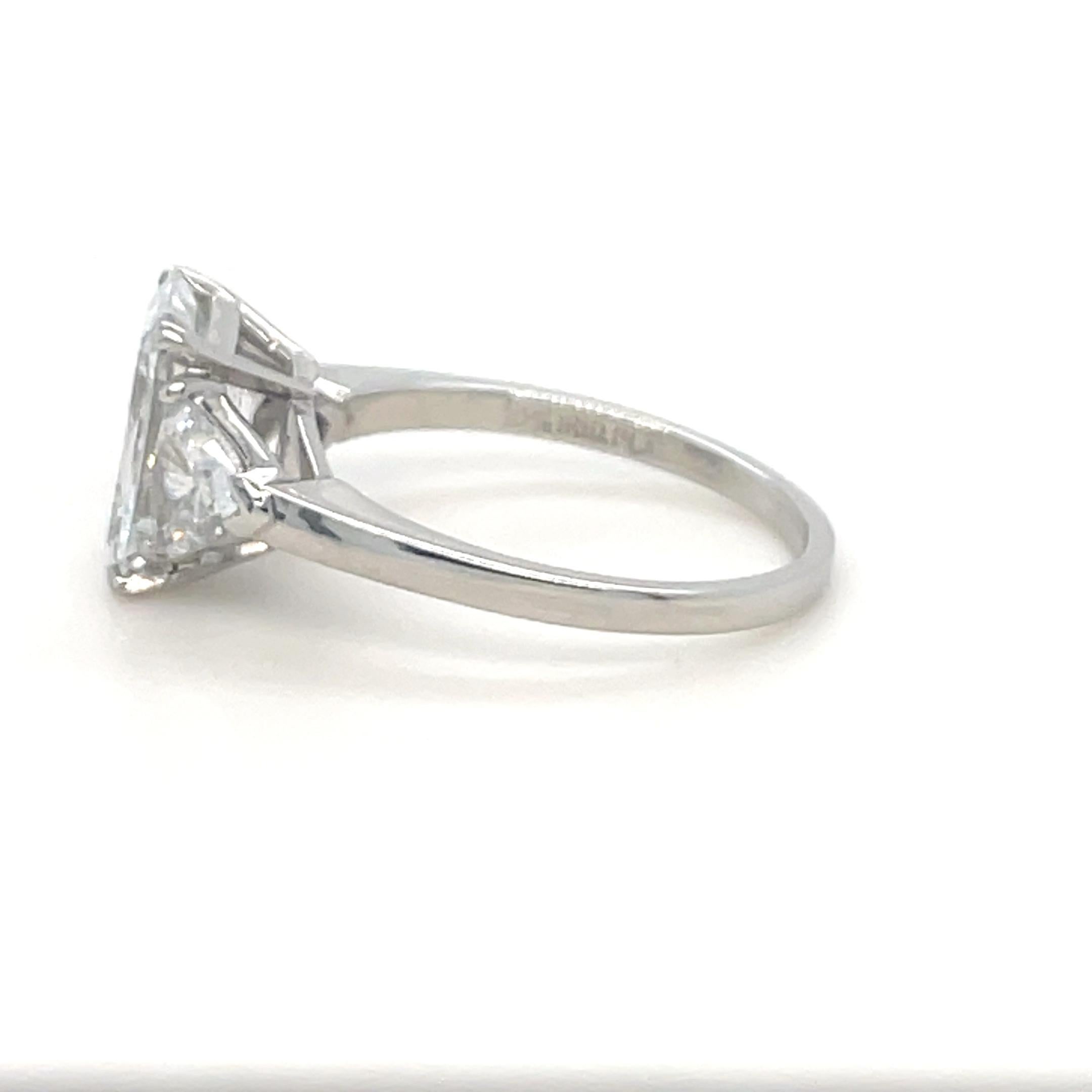 This absolutely stunning three stone diamond ring by Cartier features a 3.00 carat emerald cut diamond with F color and VS1 clarity, flanked by two trillion cut diamonds weighing approximately 1.00 carat total. Mounted in platinum and crafted with