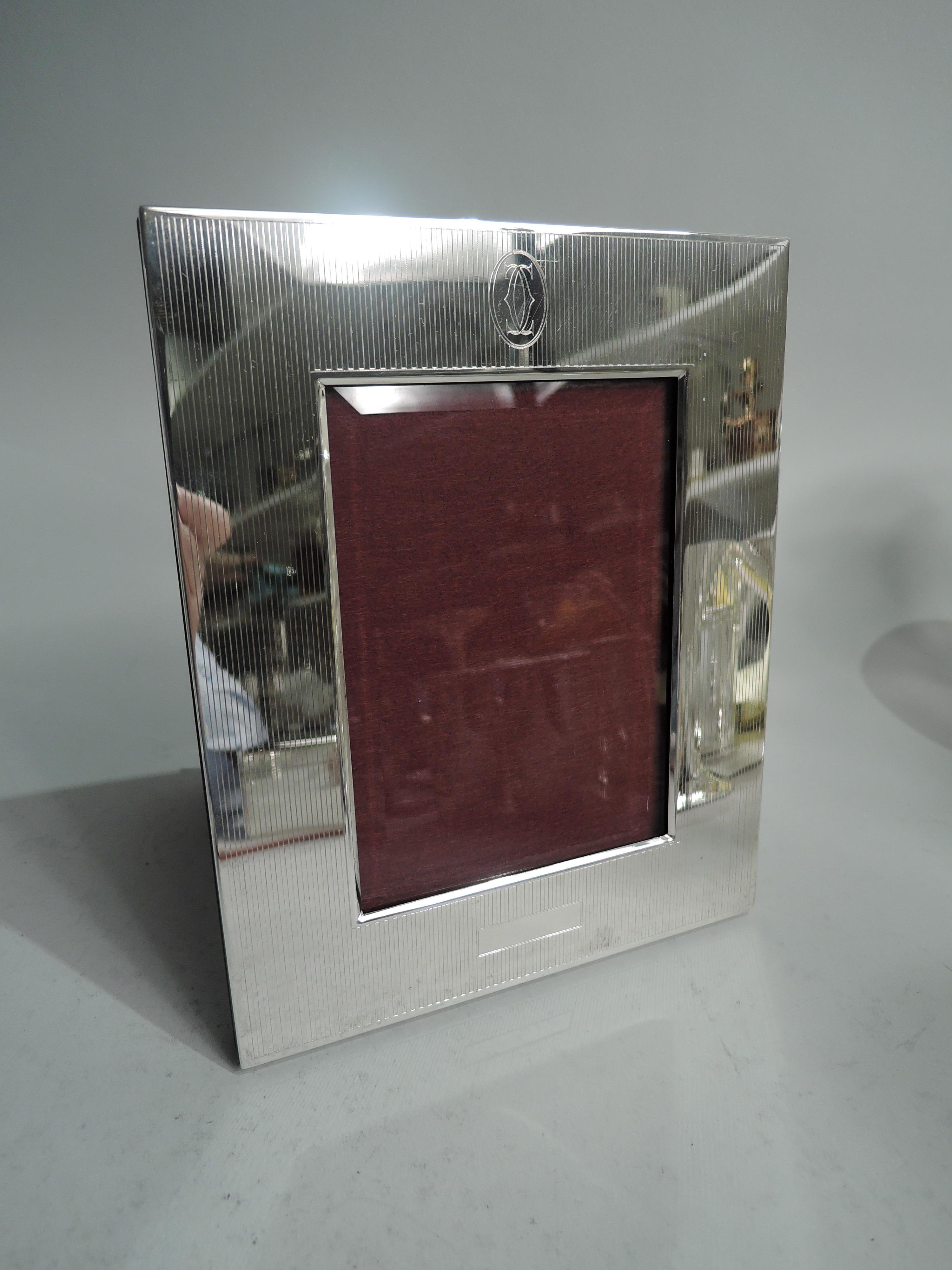 American Art Deco sterling silver picture frame, ca 1930. Retailed by Cartier in New York. Rectangular surround in wide and flat surround with engraved through lines. At top oval cartouche engraved with retailer’s symbol in form of two interlaced
