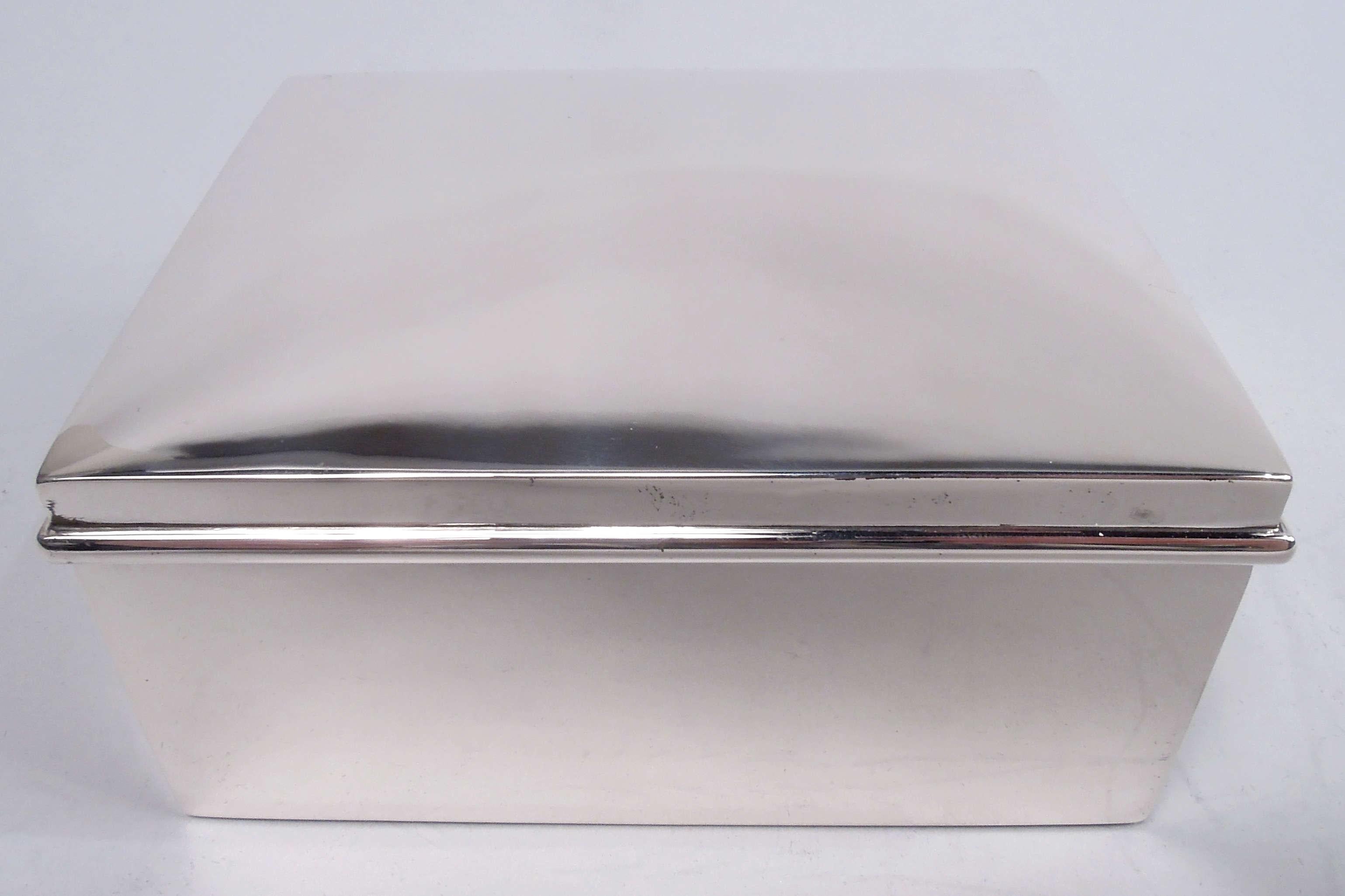 Modern sterling silver box, ca 1920. Retailed by Cartier in New York. Rectangular with straight sides. Cover hinged with curved top and overhanging rim. Interior cedar lined. Fully marked including maker’s (Ahrendt & Kautzman) and retailer’s stamps,