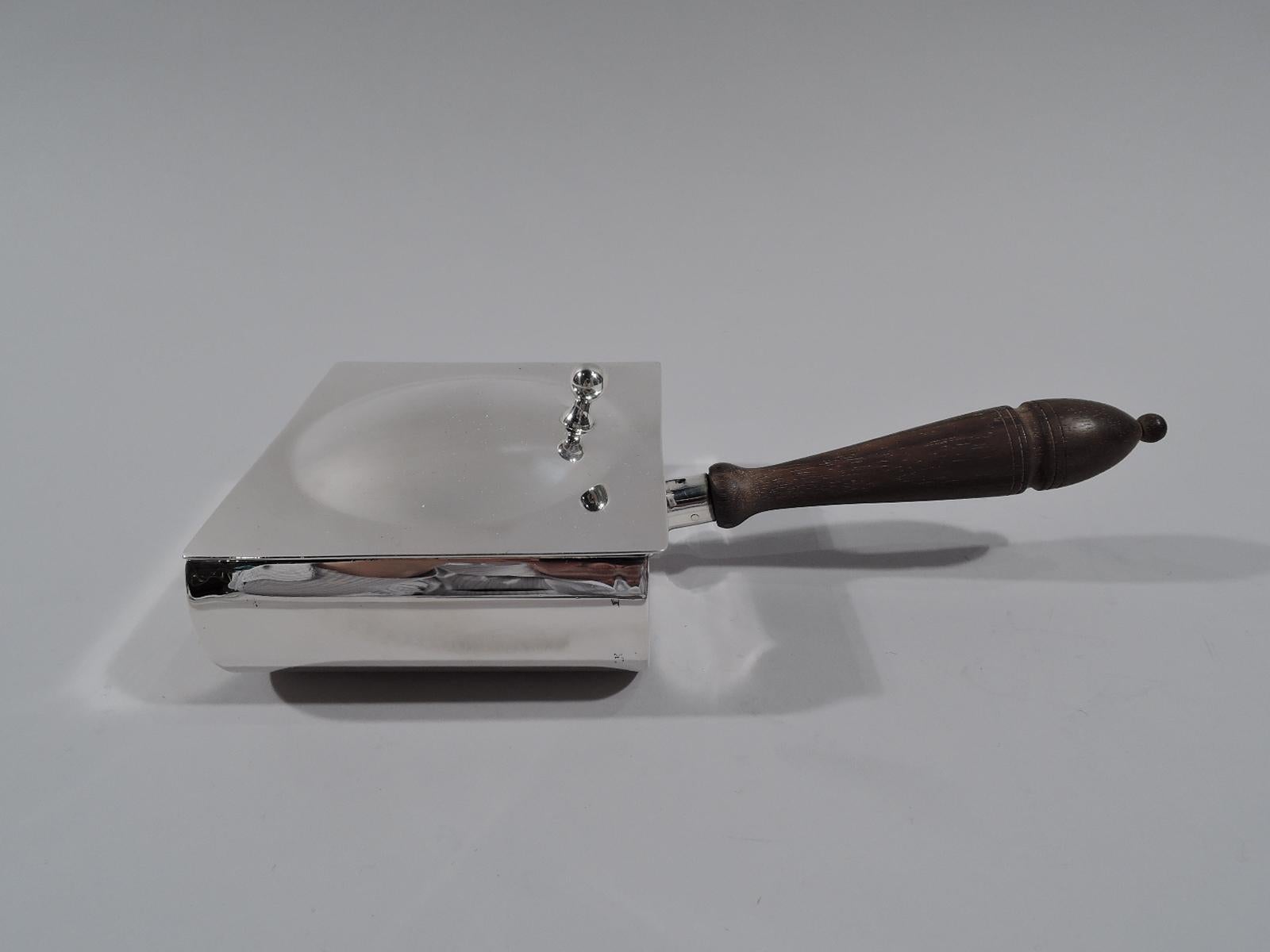 American modern sterling silver crumer, circa 1940. Retailed by Cartier in New York. Curved sides and flat ends. Cover flat and hinged; center domed with ball thumb rest. Stained-wood baluster handle. Marked “Cartier / Sterling / 29”. 

Overall