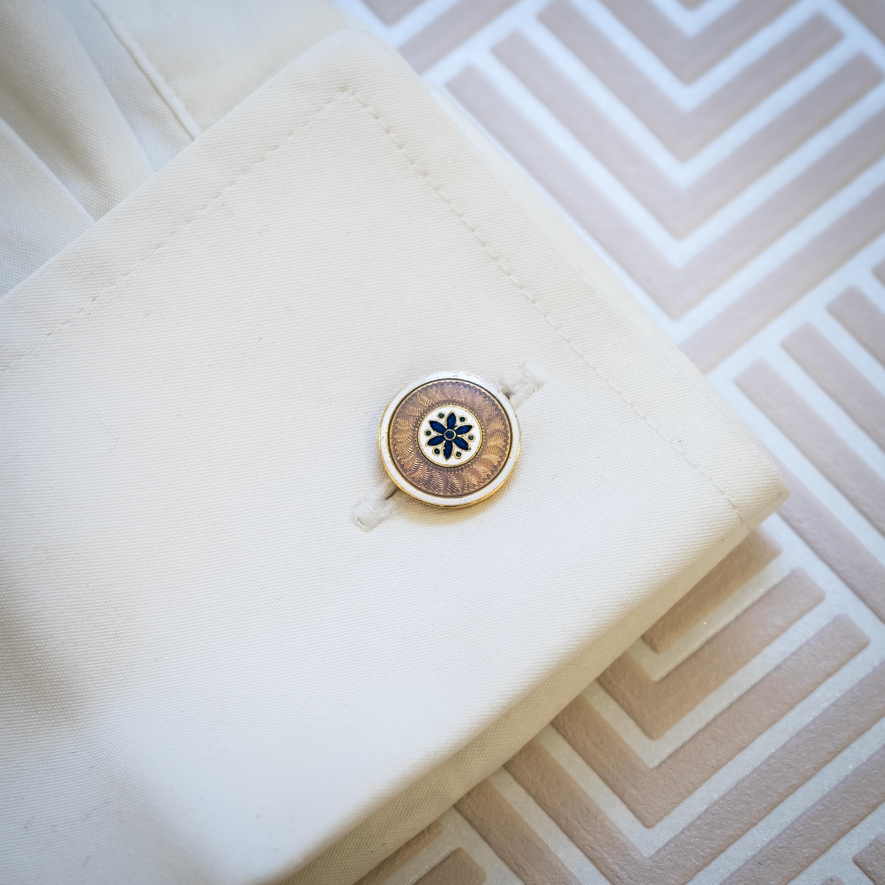A pair of Art Deco Cartier enamel cufflinks, with a central dark blue, guilloche enamel flower, with green guilloche enamel dots, between the petals, on a white enamel background, surrounded by pale grey guilloche enamel, on a background of