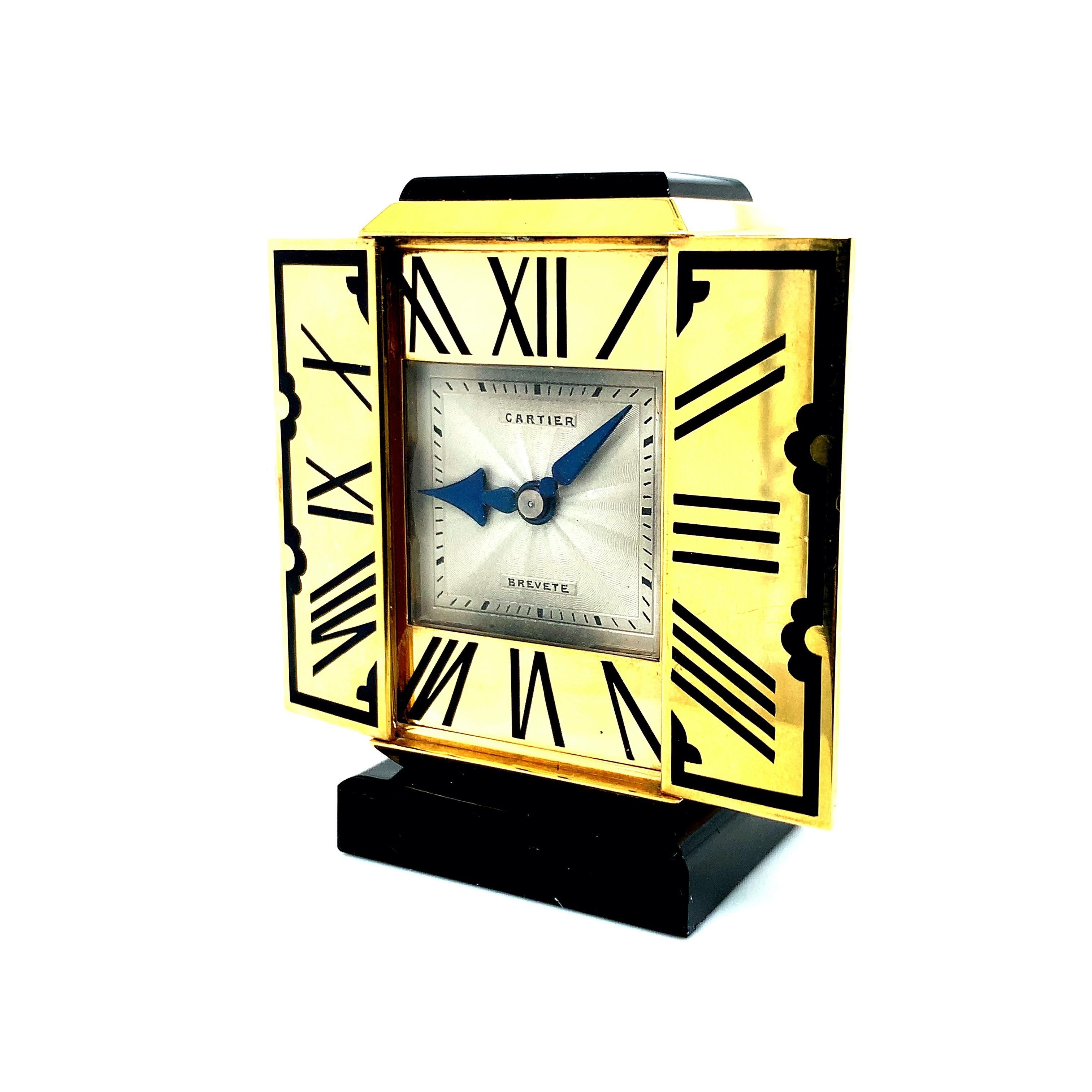 This travel clock is triptych shaped. When its doors are opened, the dial appears, which is adorned with hours in black enameled Roman numerals in an oriental style frame. The square dial in guilloché silver with railroad tracks and blued steel