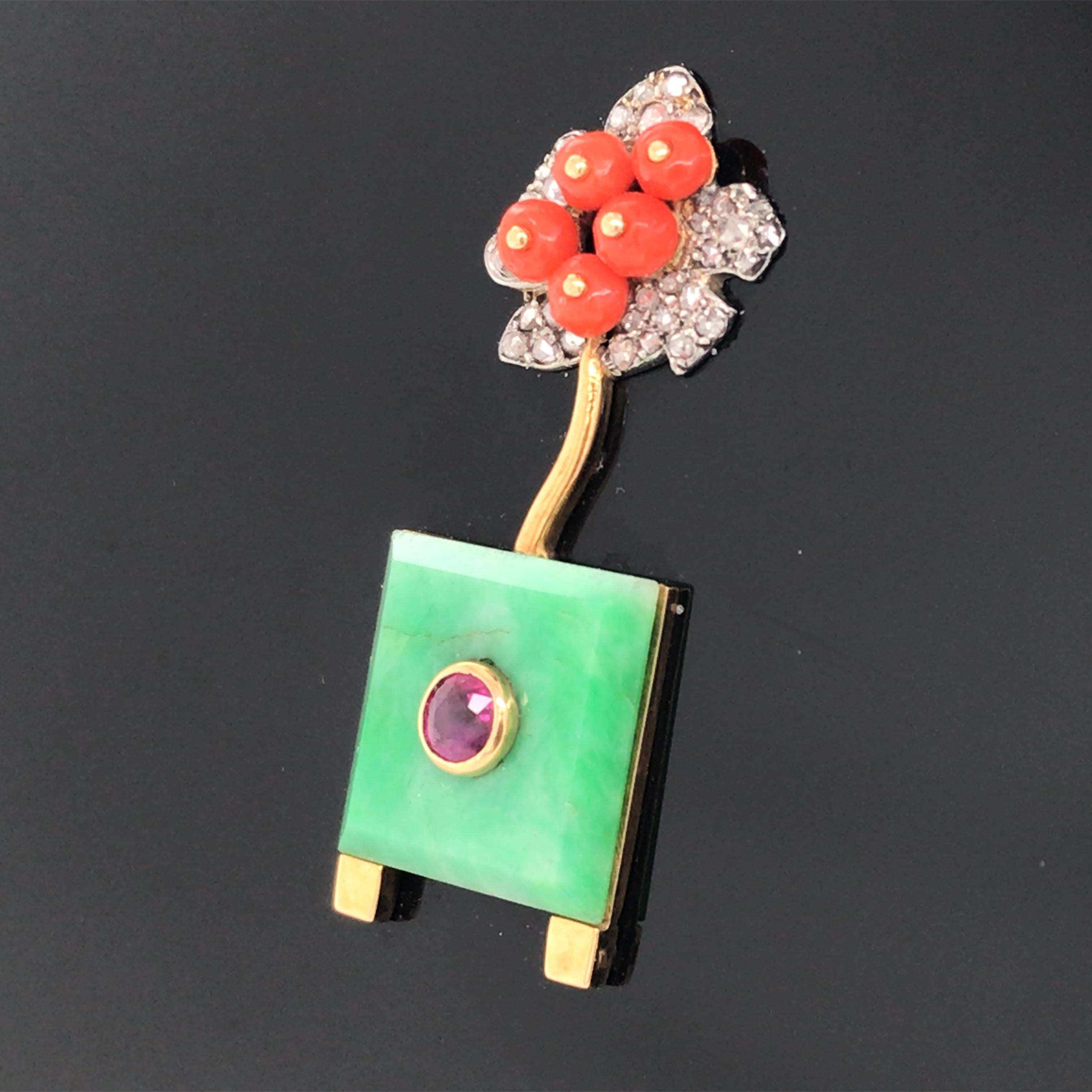 Circa 1925. Diamants taillés en rose, plaque de jade carrée, rubis rond, perles de corail, résine noire. 

Cachet : 
