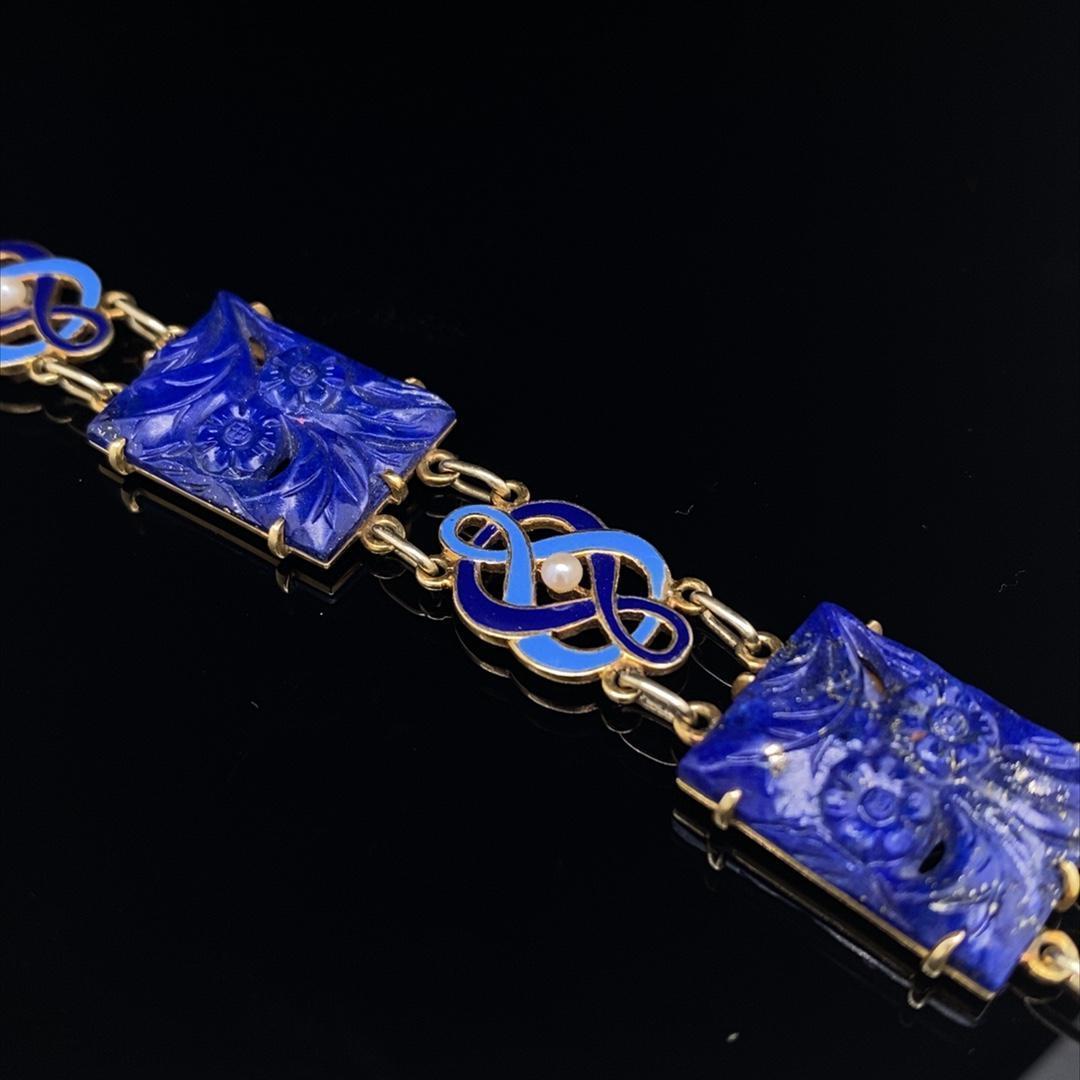 A Cartier Art Deco lapis, enamel and pearl bracelet, yellow gold.

This rare and unusual bracelet is entirely crafted in 14kt yellow gold and set with 4 hand carved plaques of lapis lazuli featuring flowers on each, interspaced with 5 enamel and