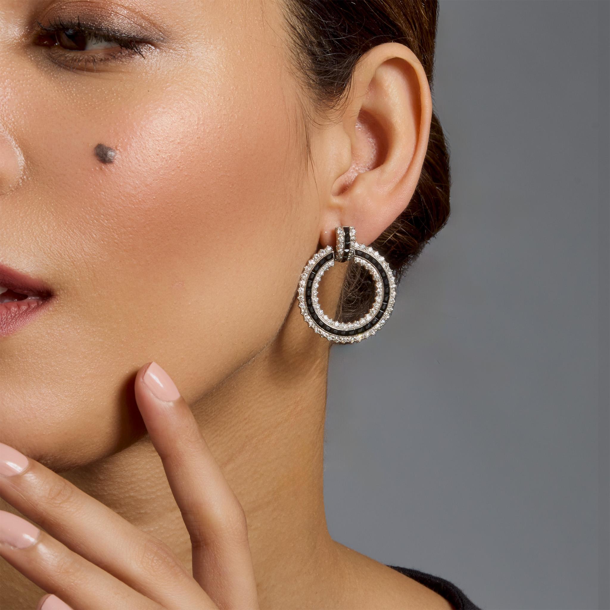 Created in France in the 1920s, these hoop earrings are set with onyx and diamonds. Each is designed as a slightly arched top suspending a free hanging circular hoop, set throughout with French-cut onyx and old single-cut diamonds, millegrain