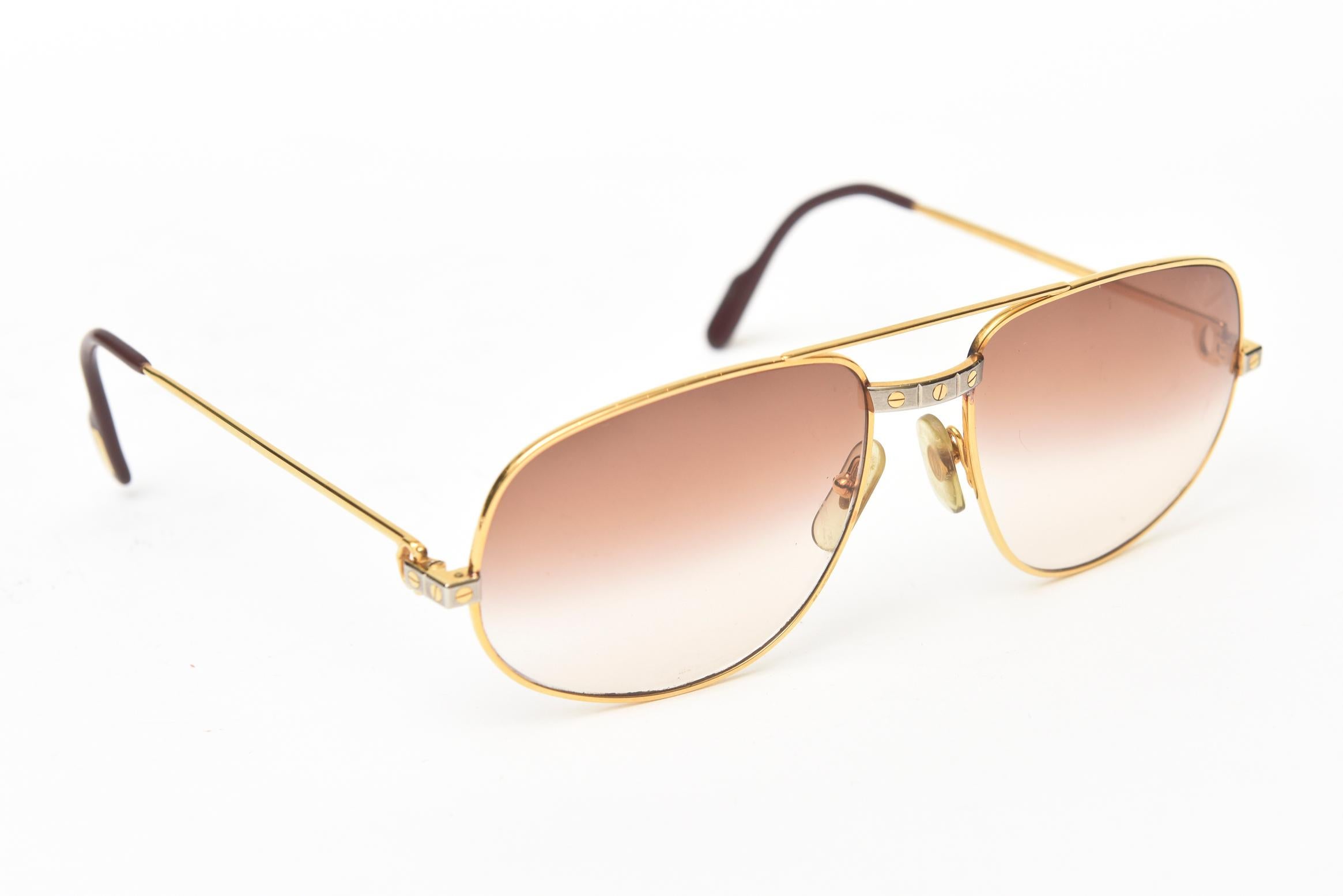 These wonderful Cartier vintage aviator sunglasses are called Santos. They are with the light brown UV protection lenses. They are 18K gold. Cartier They have burgundy red enamel ear paddles. These are classic with yellow and white gold sides. They