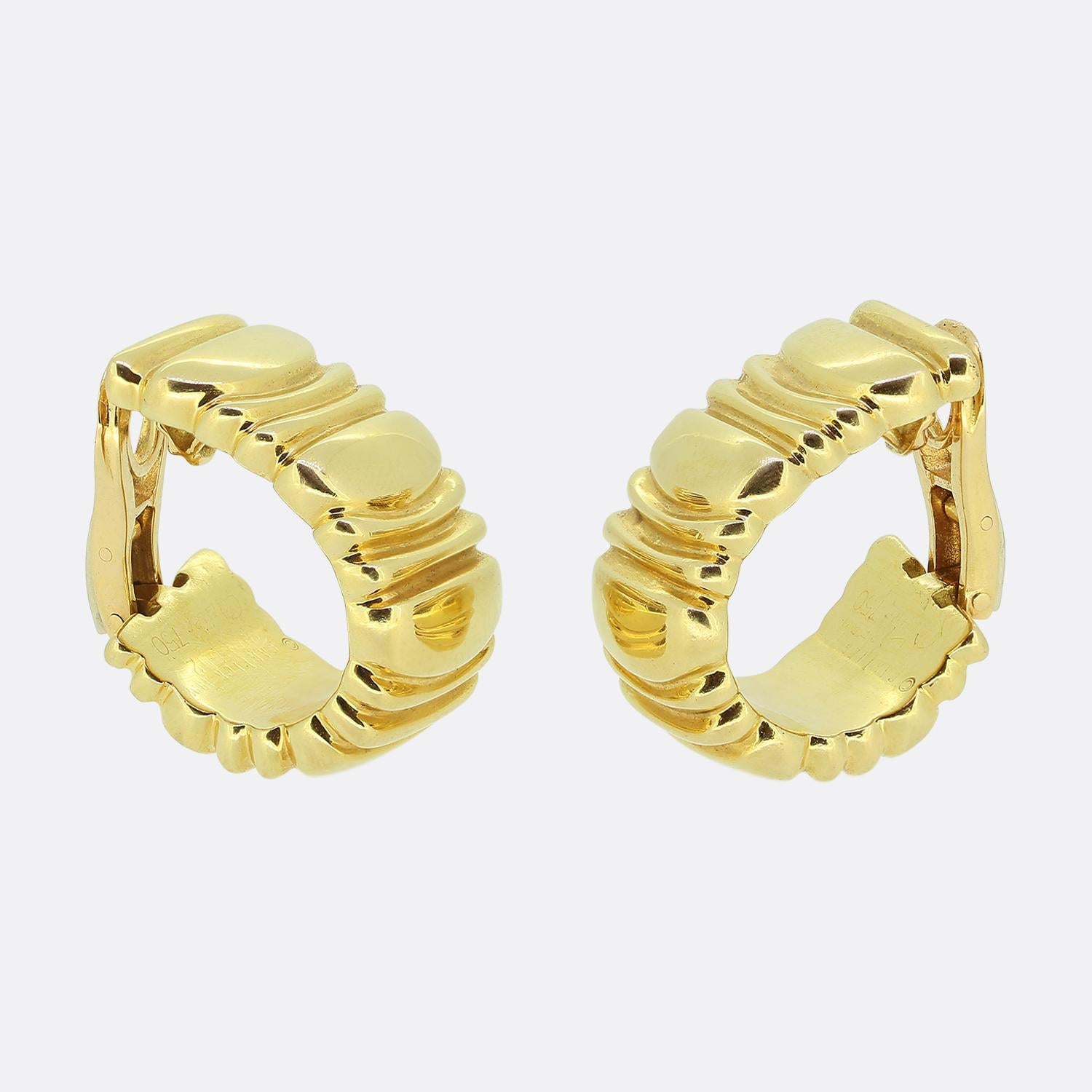 Aquí tenemos un par de elegantes pendientes de aro de la mundialmente conocida casa de joyas Cartier. Cada pendiente está fabricado en cálido oro amarillo de 18 ct y presenta un atrevido diseño acanalado. La superficie es lisa y pulida, creando un