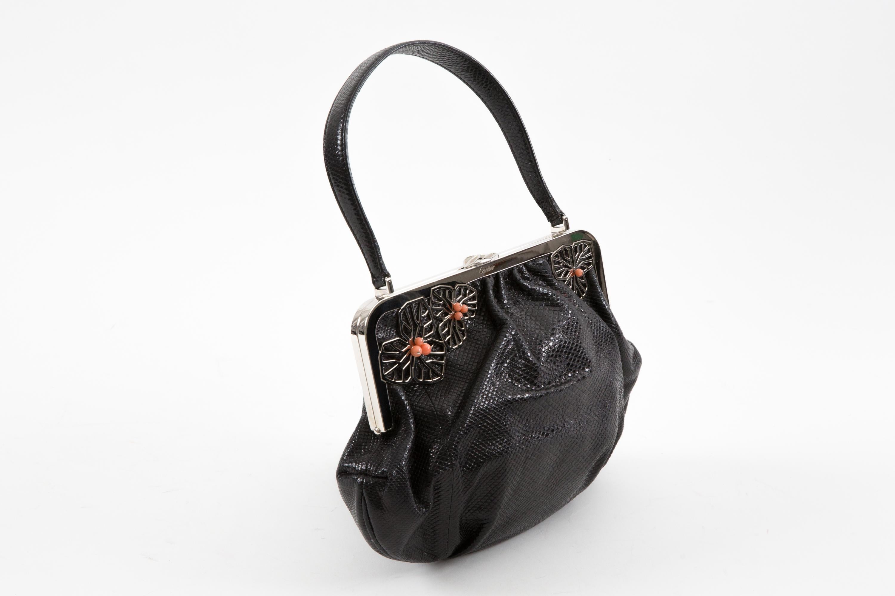 Cartier Black leather evening handbag featuring floral embellishments, silver tone hardware with top frame closure and silver lambskin leather lining with inner slip pocket. 
Circa 2000s  Made in France.
In good vintage condition. 
Length: 9.05in.