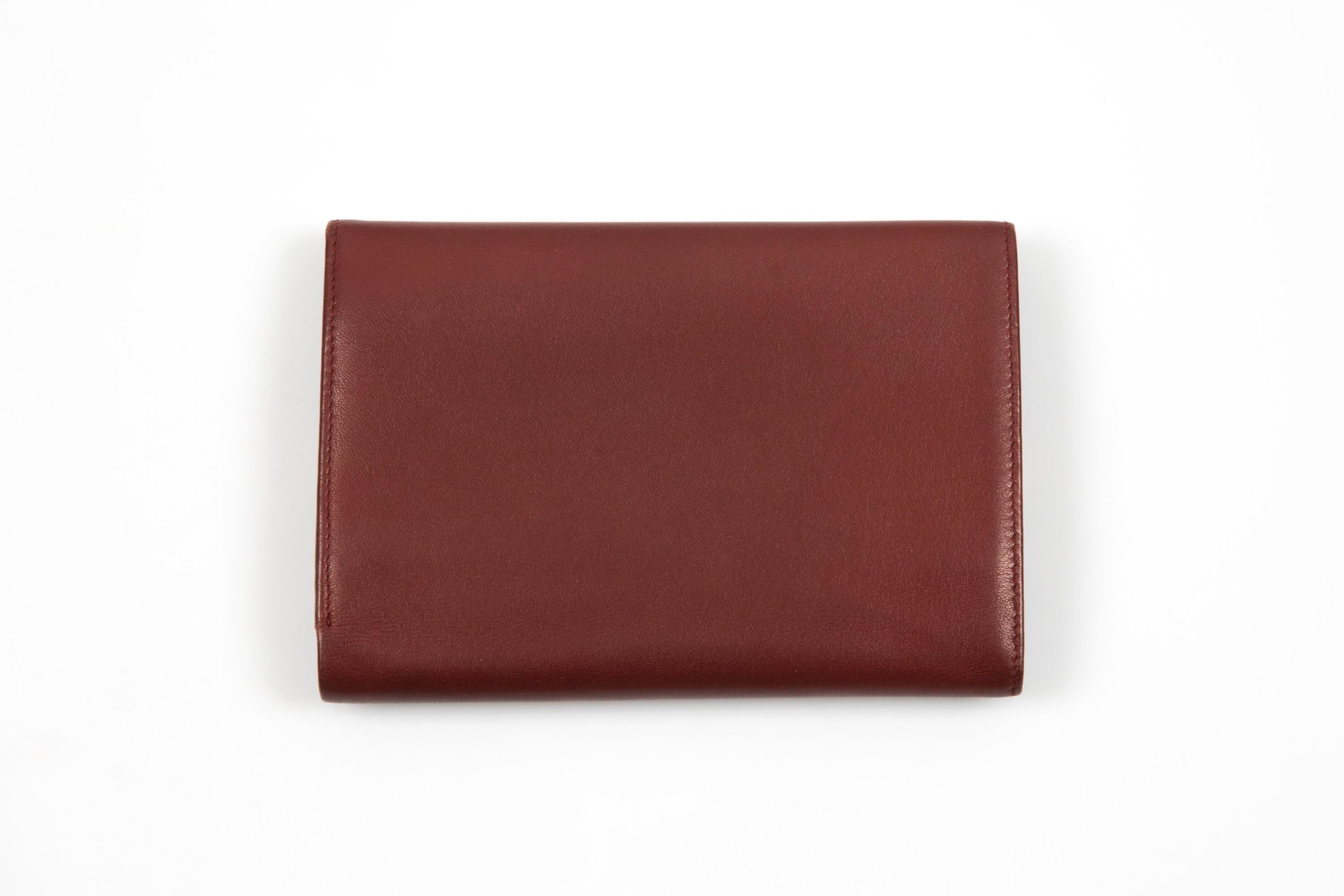 Cartera Cartier Burdeos grande de piel con esquinas exteriores doradas, logotipo exterior en relieve, compartimento monedero trasero con abertura de solapa dorada, compartimentos interiores y firma Cartier dorada estampada en caliente. 
Circa: años