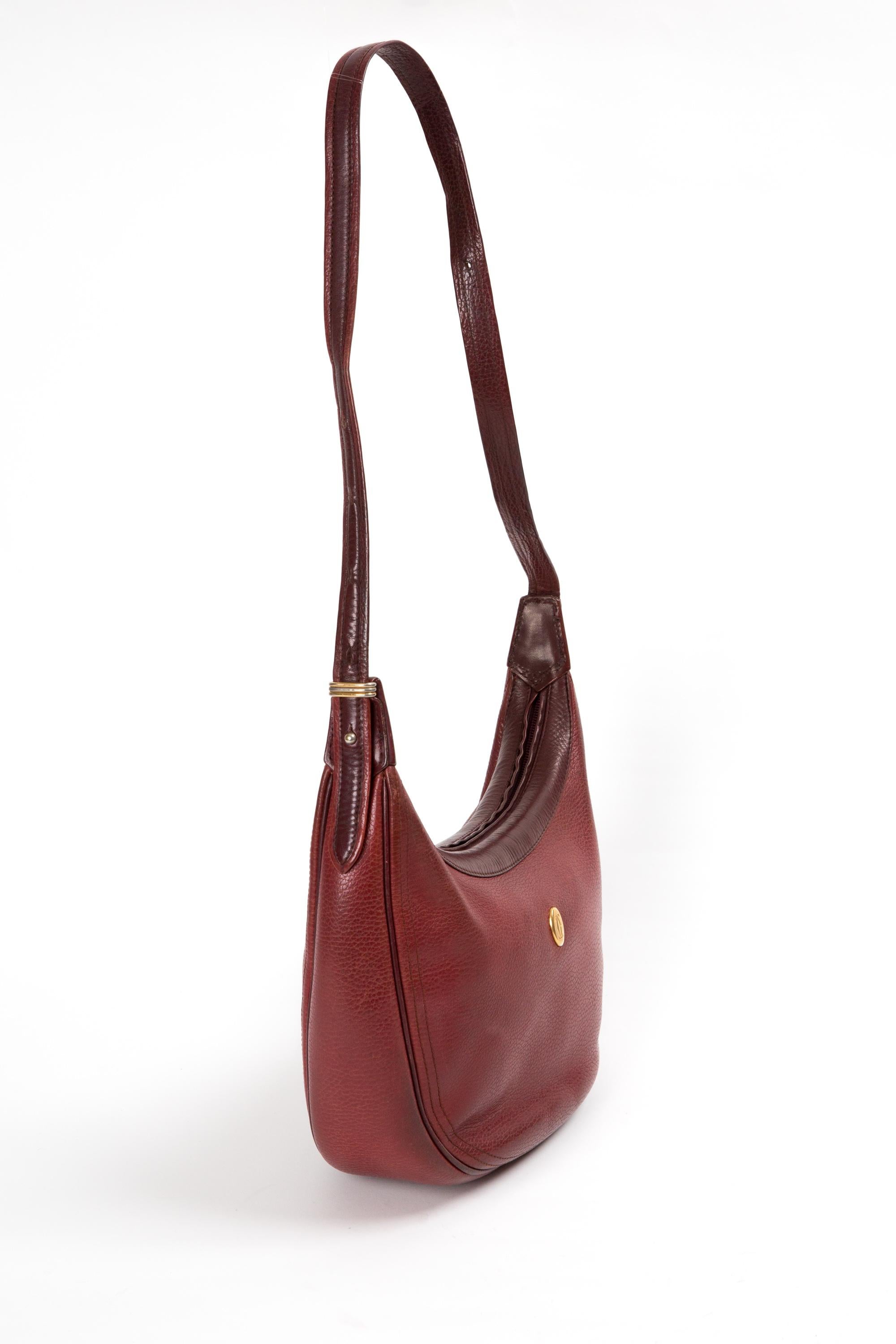 Cartier bordeaux leather crossbody messenger bag featuring an half-moon shape, front gold-tone logo at front, top zip opening, shoulder strap (29.5in. (75cm)), a logo lining, an inside zip pocket, inside logo stamp. 
Circa 1990s 
Made in France.
In