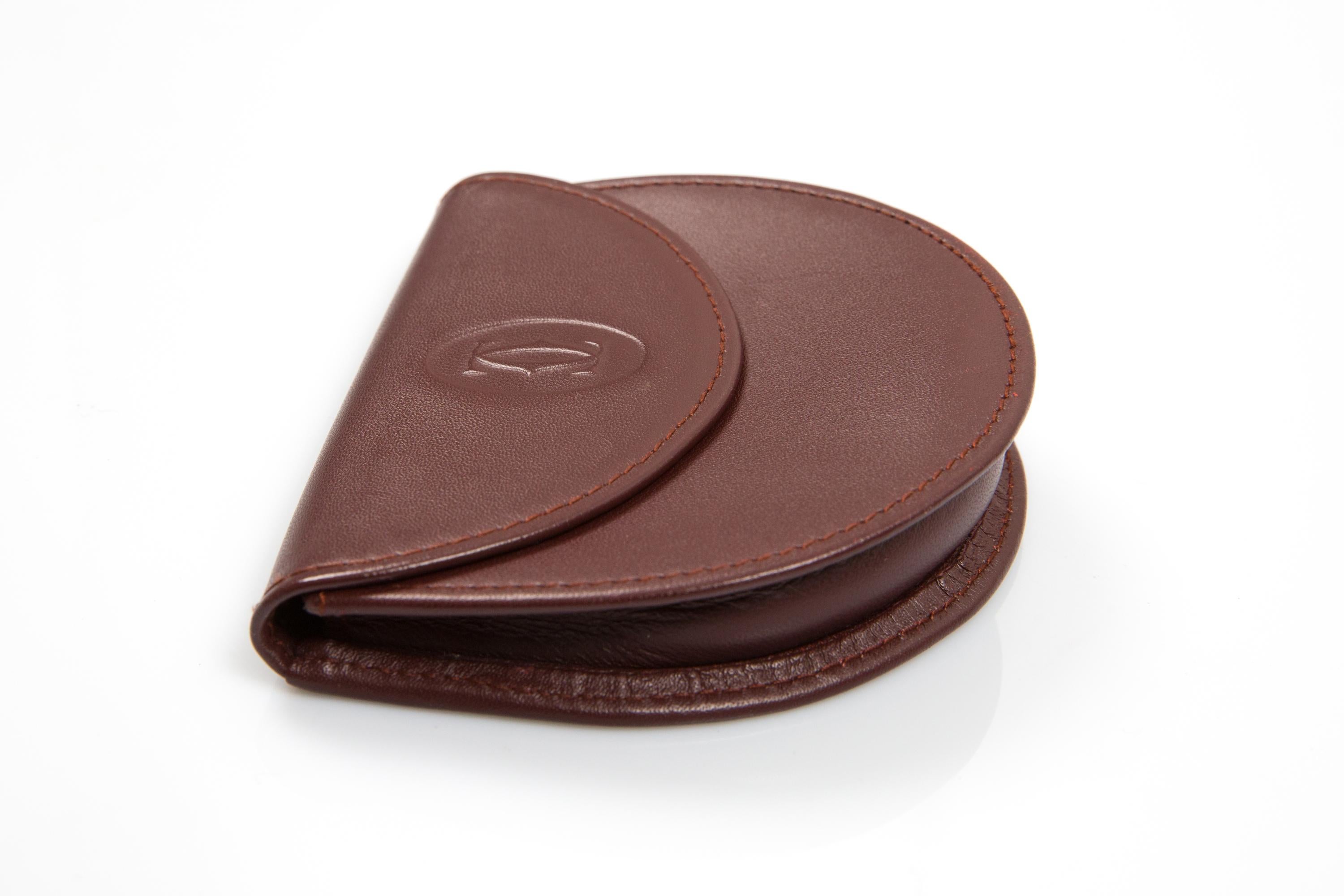 Coffret à monnaie demi-lune en cuir bordeaux de Cartier avec  un logo extérieur en relief, une fermeture à pression avec logo, une petite pochette au dos et une signature intérieure de Cartier estampillée à chaud. 
Circa : 1990
En bon état vintage.