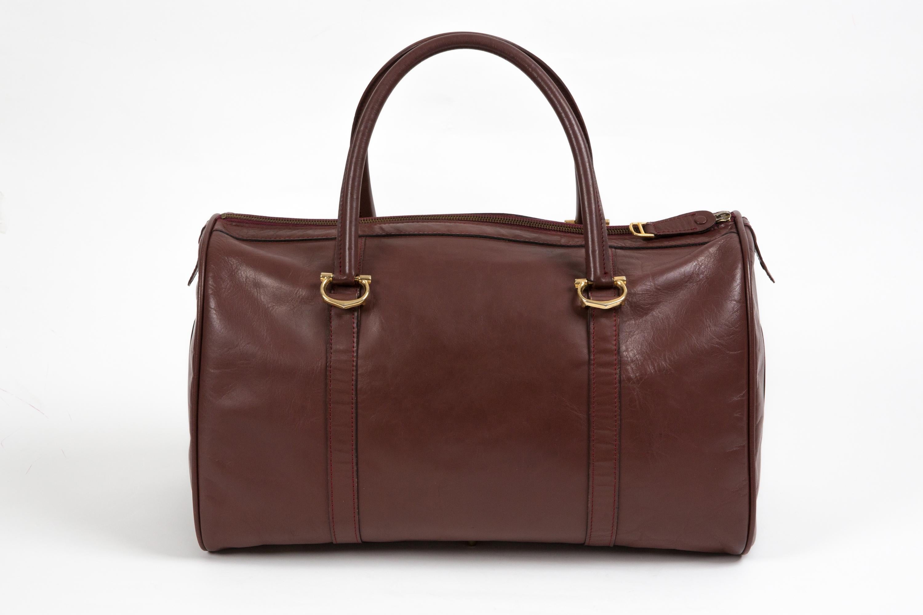 Cartier Bordeaux leather Large Week-End Bag featuring top round leather handles, gold-plated hardware, a top zipper closure, set keys, clochette and padlock, large embossed logo at sides, inside zipped pocket and logo plaque. 
Circa 1980s  
In good