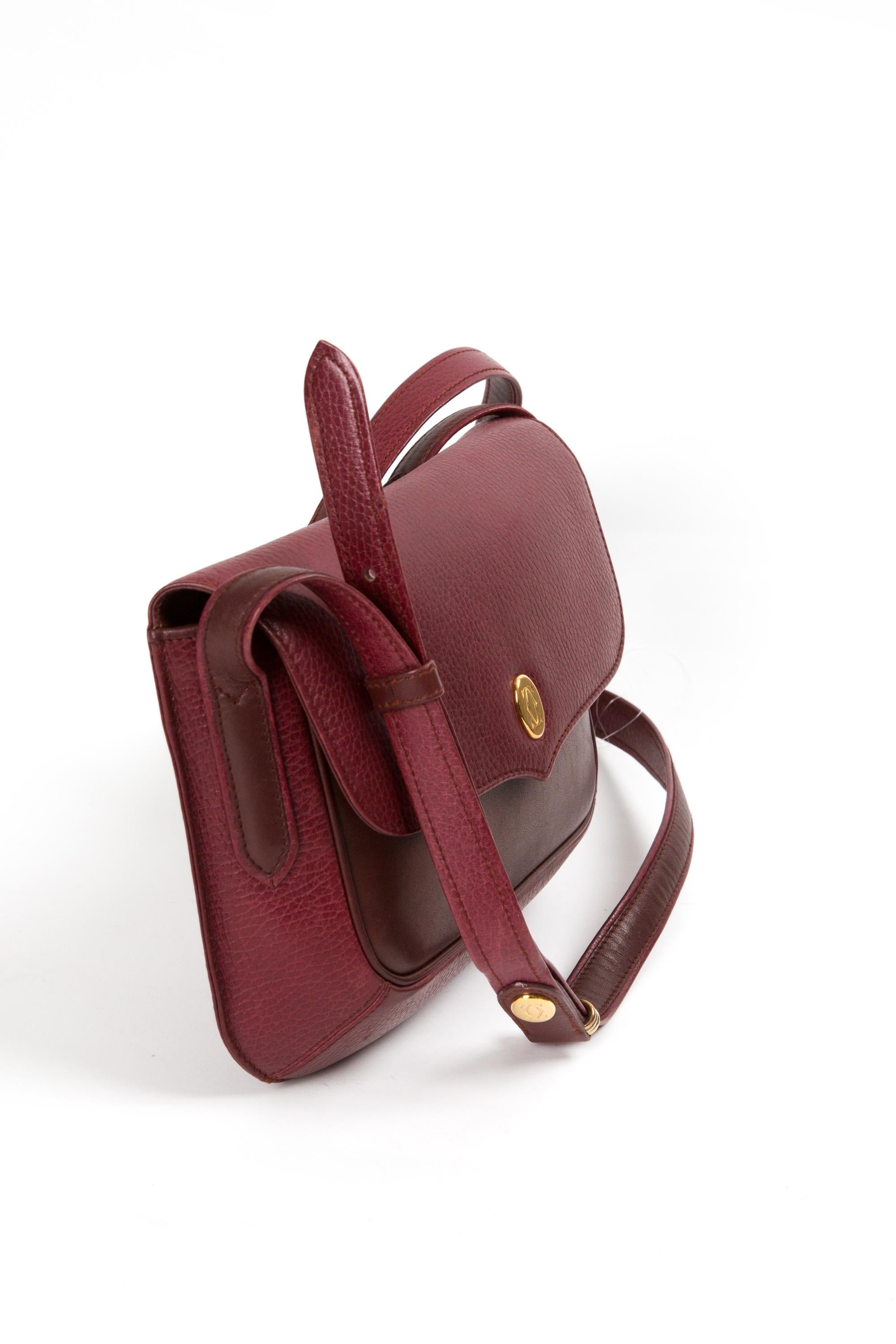 Bolso bandolera de piel burdeos de Cartier con placa delantera dorada con logotipo y cierre a presión debajo, correa ajustable para el hombro y cierre de hebilla, compartimentos interiores, un bolsillo interior con cremallera y placa interior dorada
