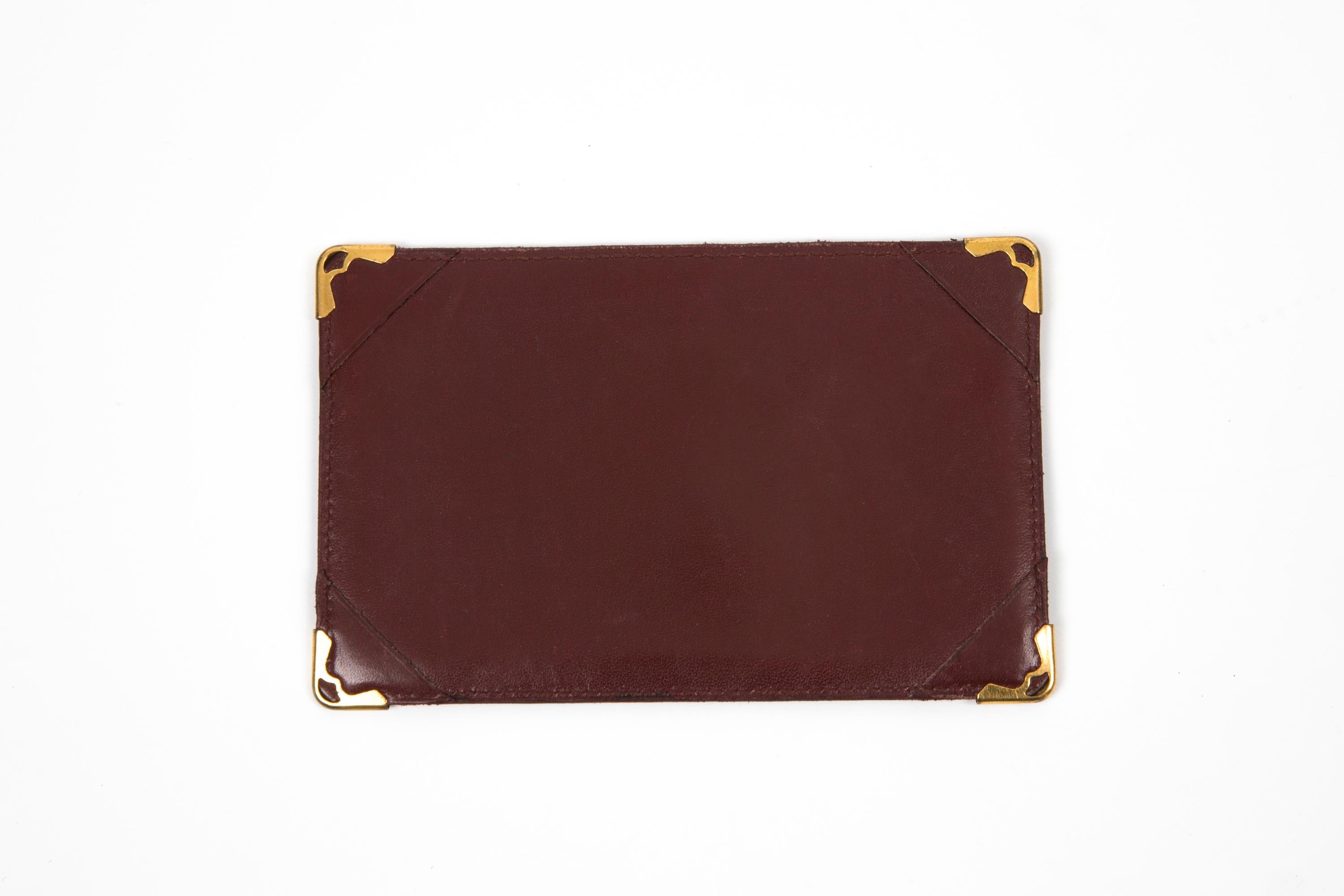 Cartier Bordeaux leather simple card holder featuring one large central slot, gold-plated corners, and a golden hot-stamped Cartier signature. 
Circa: 1990s
In good vintage condition. Made in France.
5.5in. (14cm) X 3.5in. (9cm) X 0.39in (1cm)
We