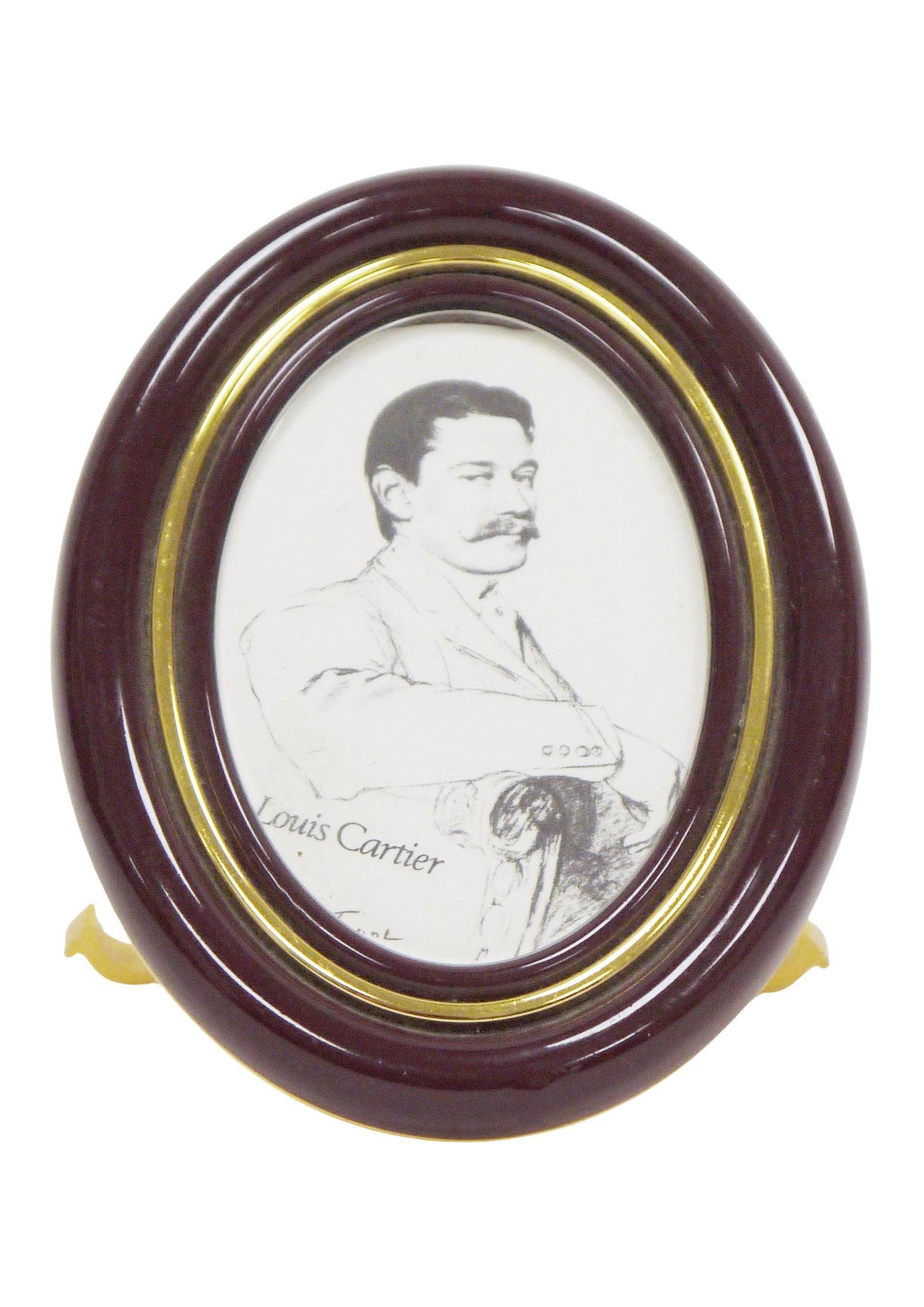A Cartier easel back photograph frame, of oval form, in a brown enamel and gold-plated frame, serial no. 8509 23218, 9cm high, fitted in a red Cartier case


