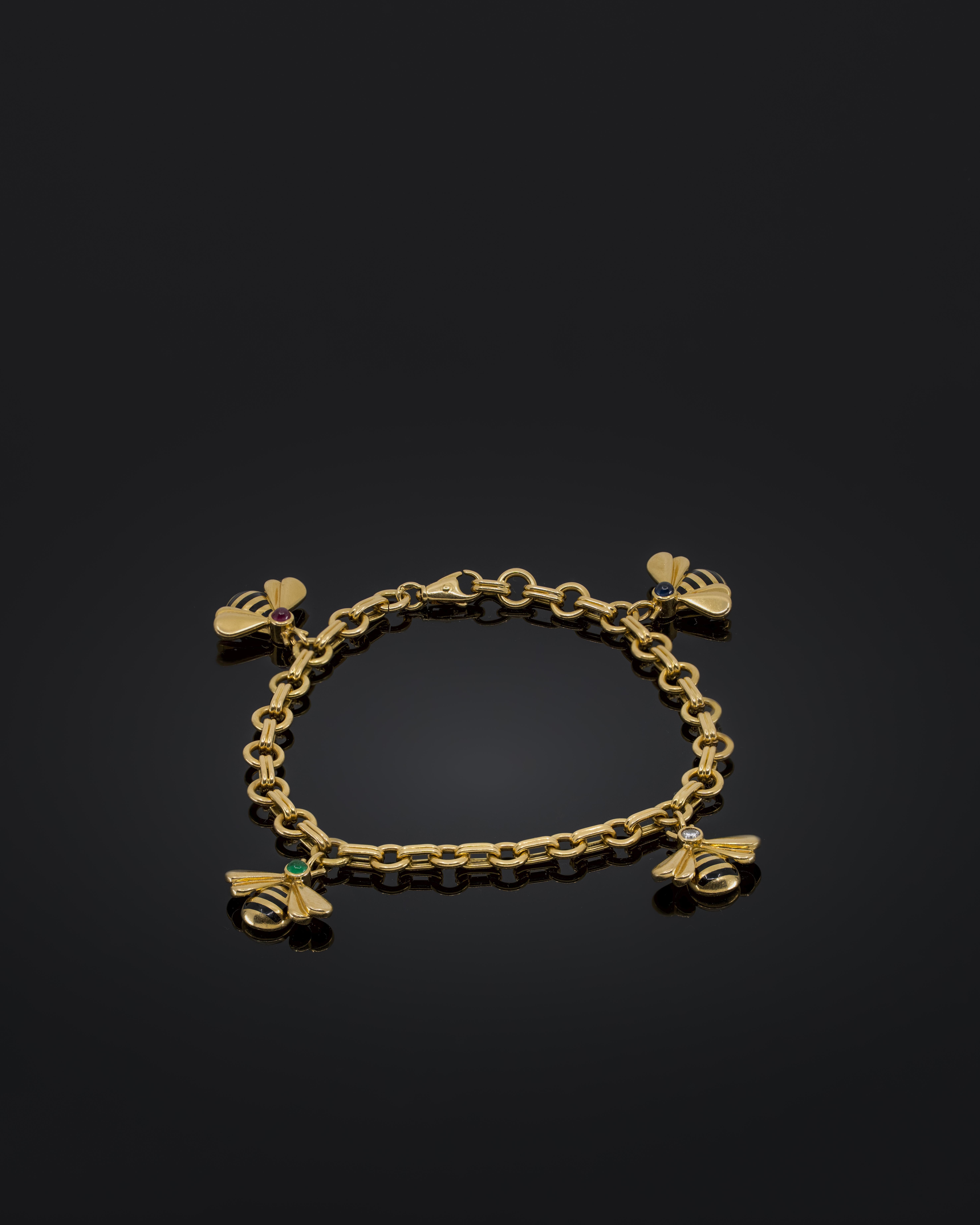 The Cartier Bumble Bee Charm Bracelet is a refined piece of jewelry from the 1990s, crafted in 18k yellow gold.

The design features four detailed bumblebee charms, each decorated with enameled stripes and set with precious gemstones such as